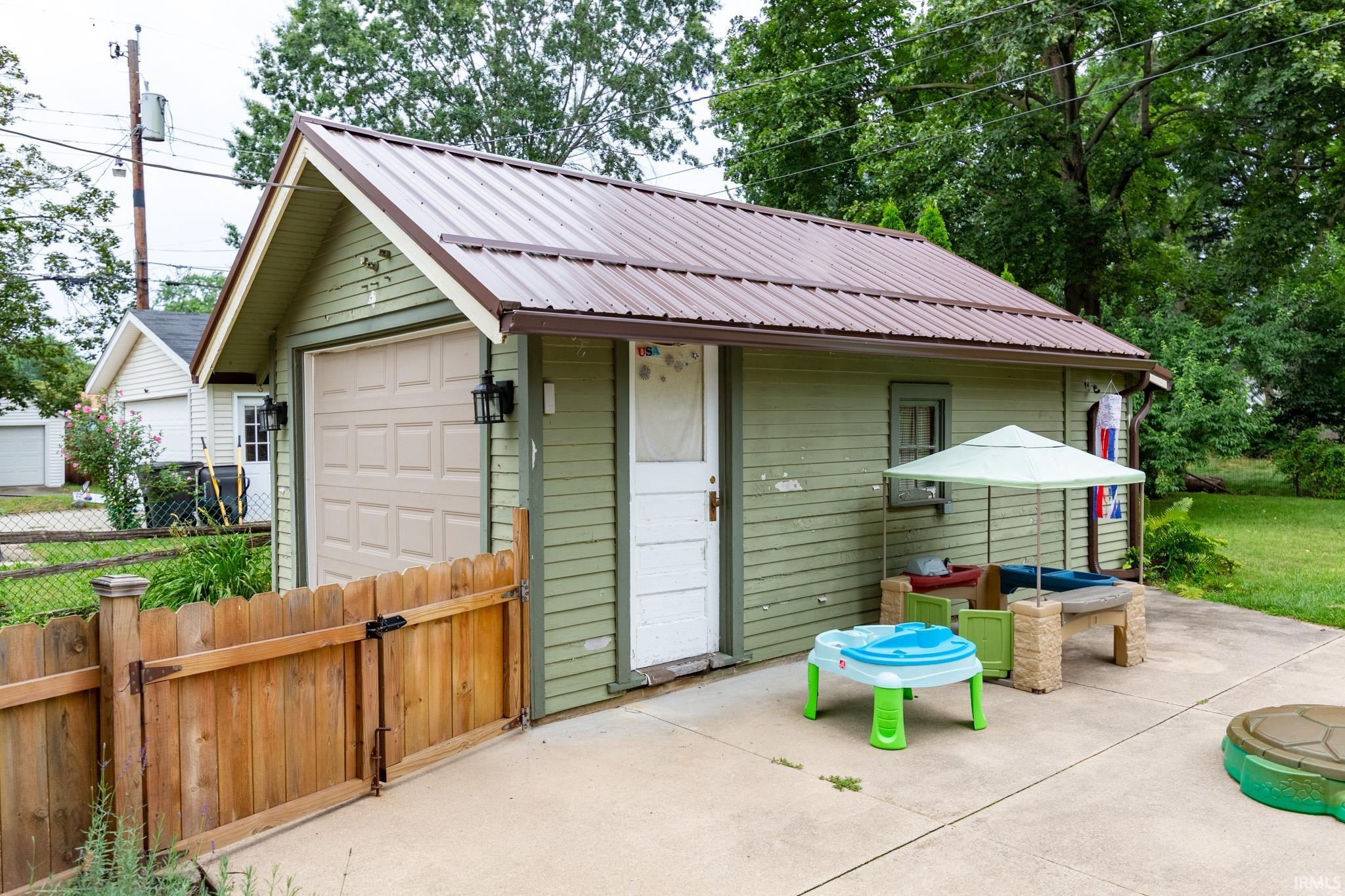 Detached garage structure featuring a brown metal roof, light green siding, and a tan panel garage door