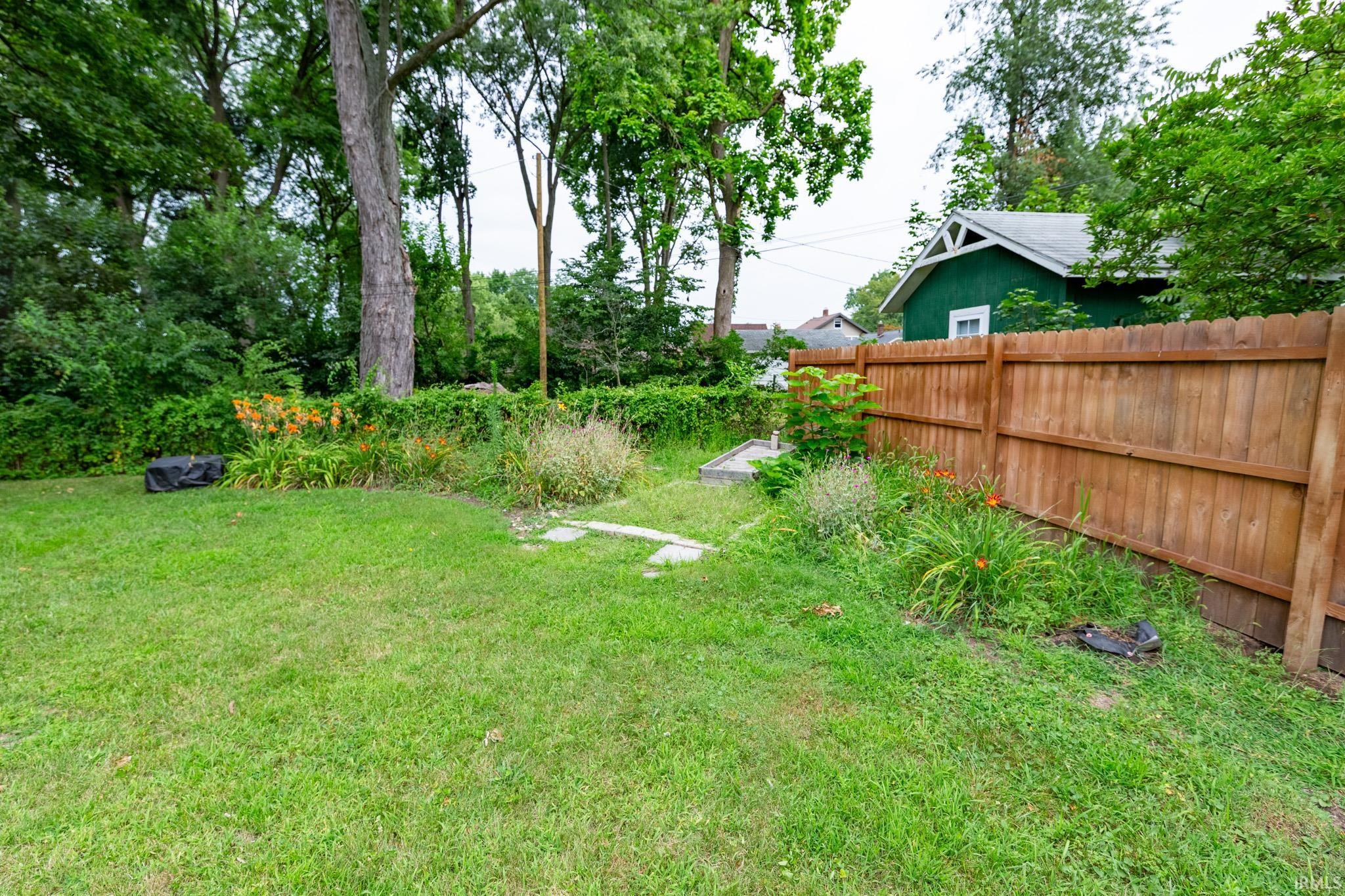 Spacious backyard featuring a manicured lawn, established garden beds, mature trees, and a privacy fence