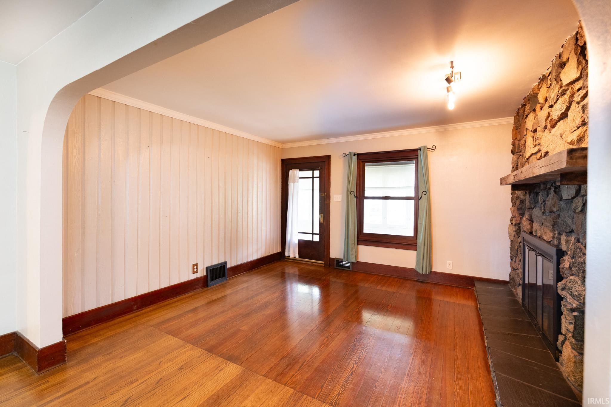 Living space featuring a stone-clad fireplace with a wood mantel, rich wood-finish flooring, and a glass-paneled entry door