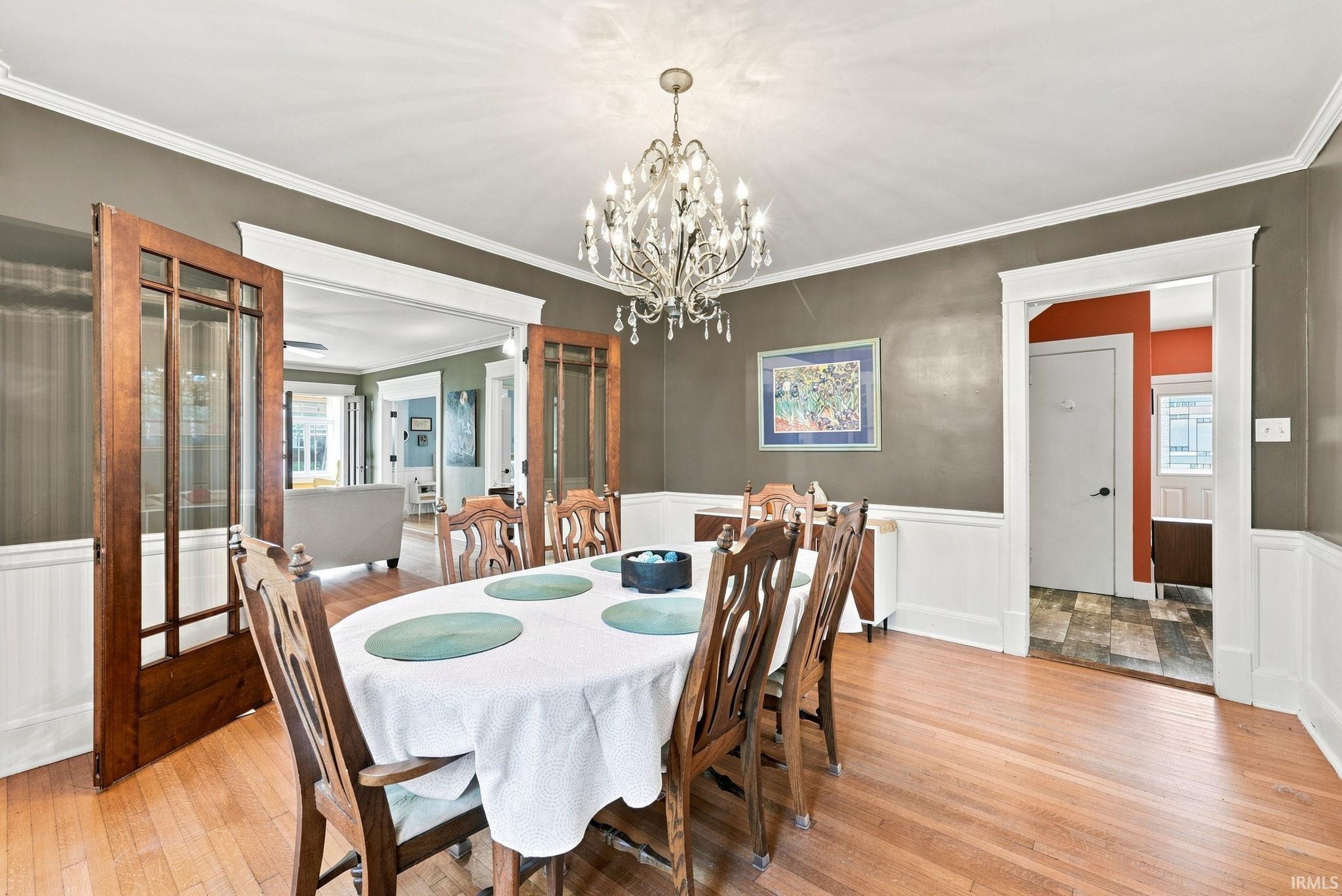 Dining area featuring wood-finish flooring, white wainscoting, and crown molding