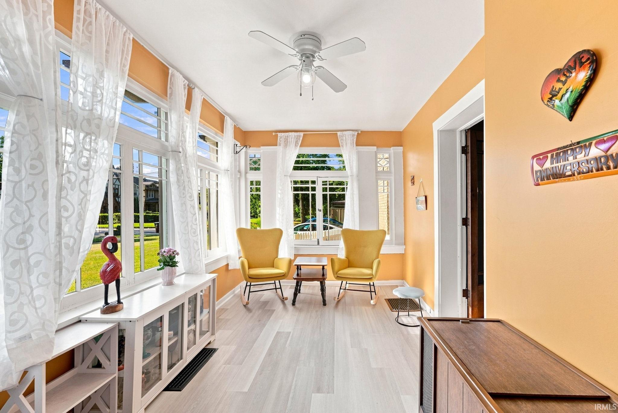 Sunroom featuring extensive window-lined walls, light wood-finish flooring, a white ceiling fan, and a built-in white media console