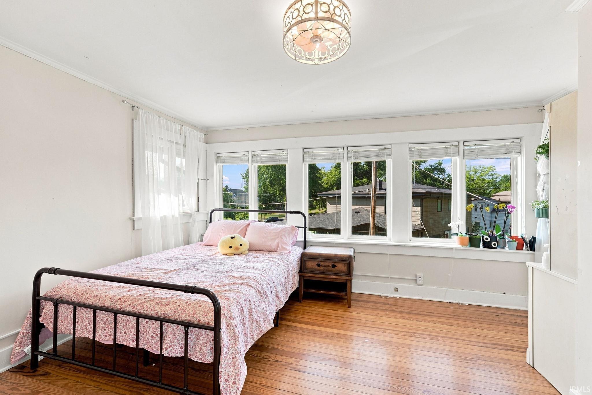 Bright room featuring wood-finish flooring, white walls, and crown molding