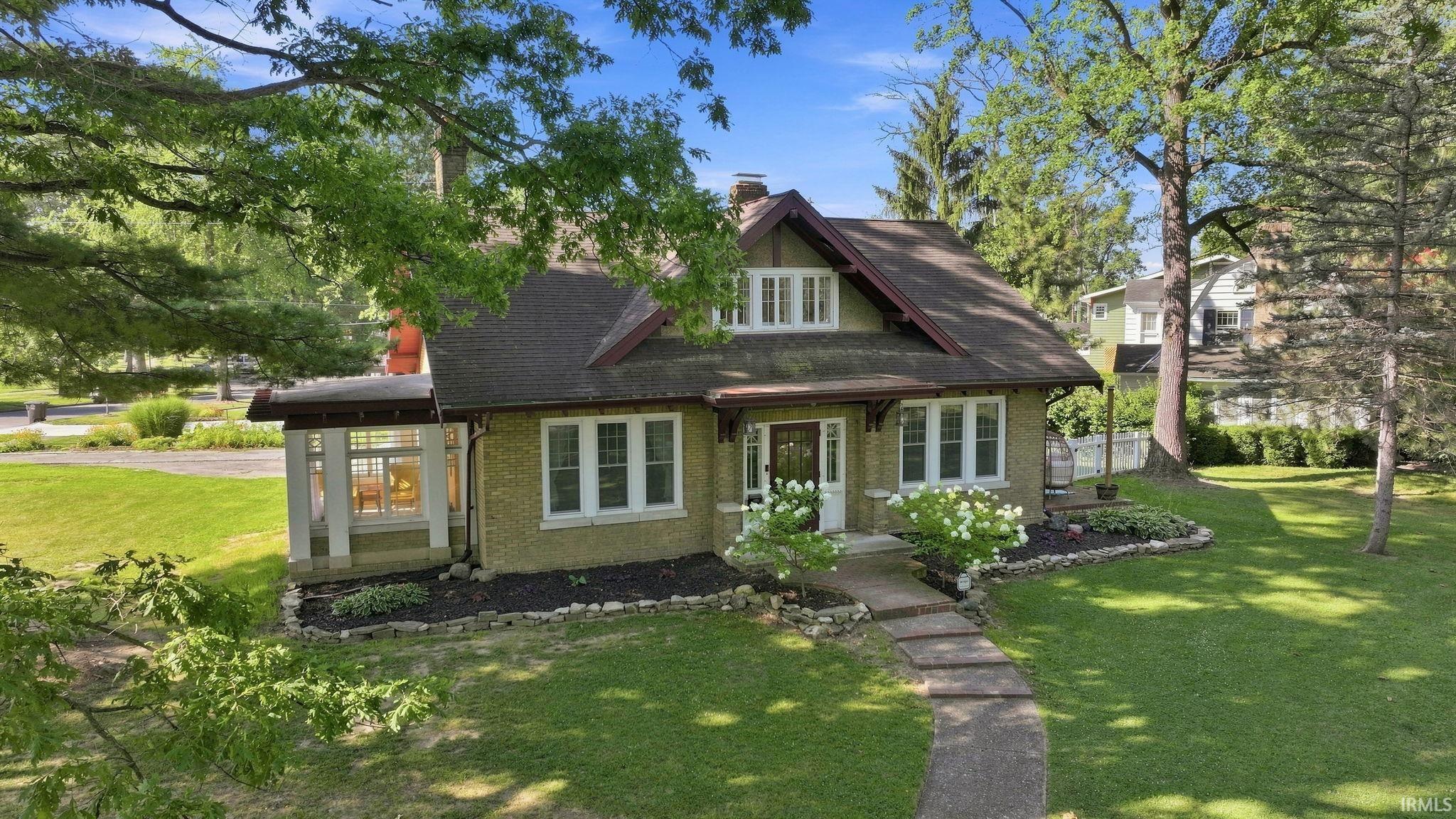Craftsman-style home featuring a stone pathway, mature trees, and a well-maintained lawn