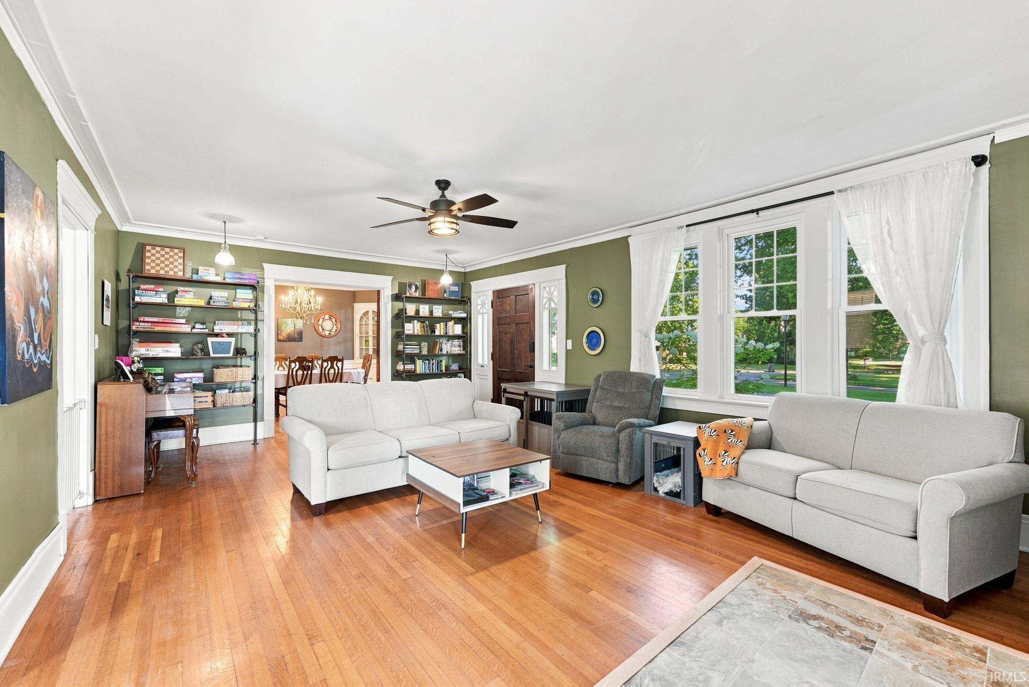 Spacious living area featuring polished wood-finish flooring, a ceiling fan with integrated lighting, and multiple large windows