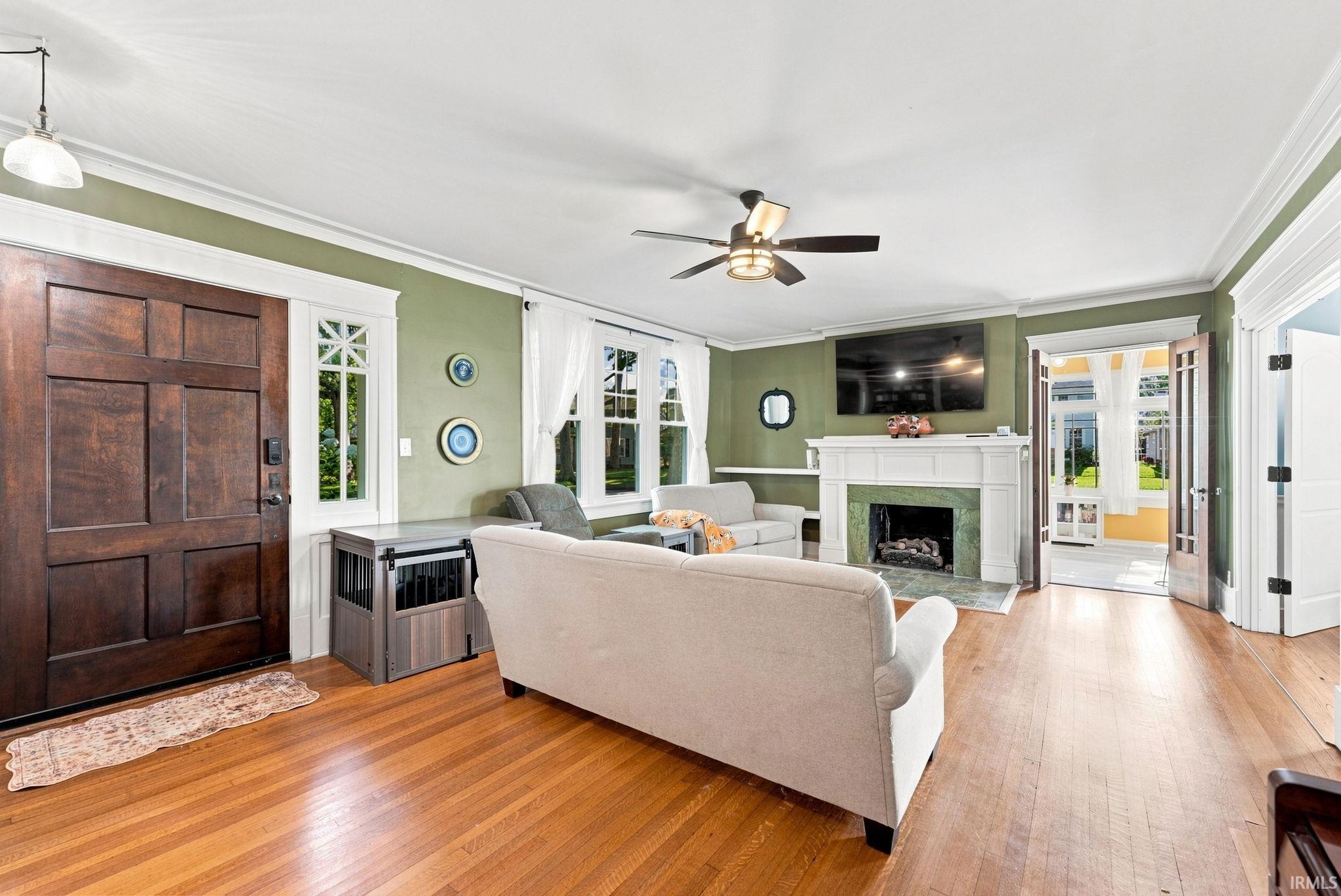 Spacious living area featuring wood-finish flooring, a decorative fireplace with a mantel and stone surround, and a ceiling fan