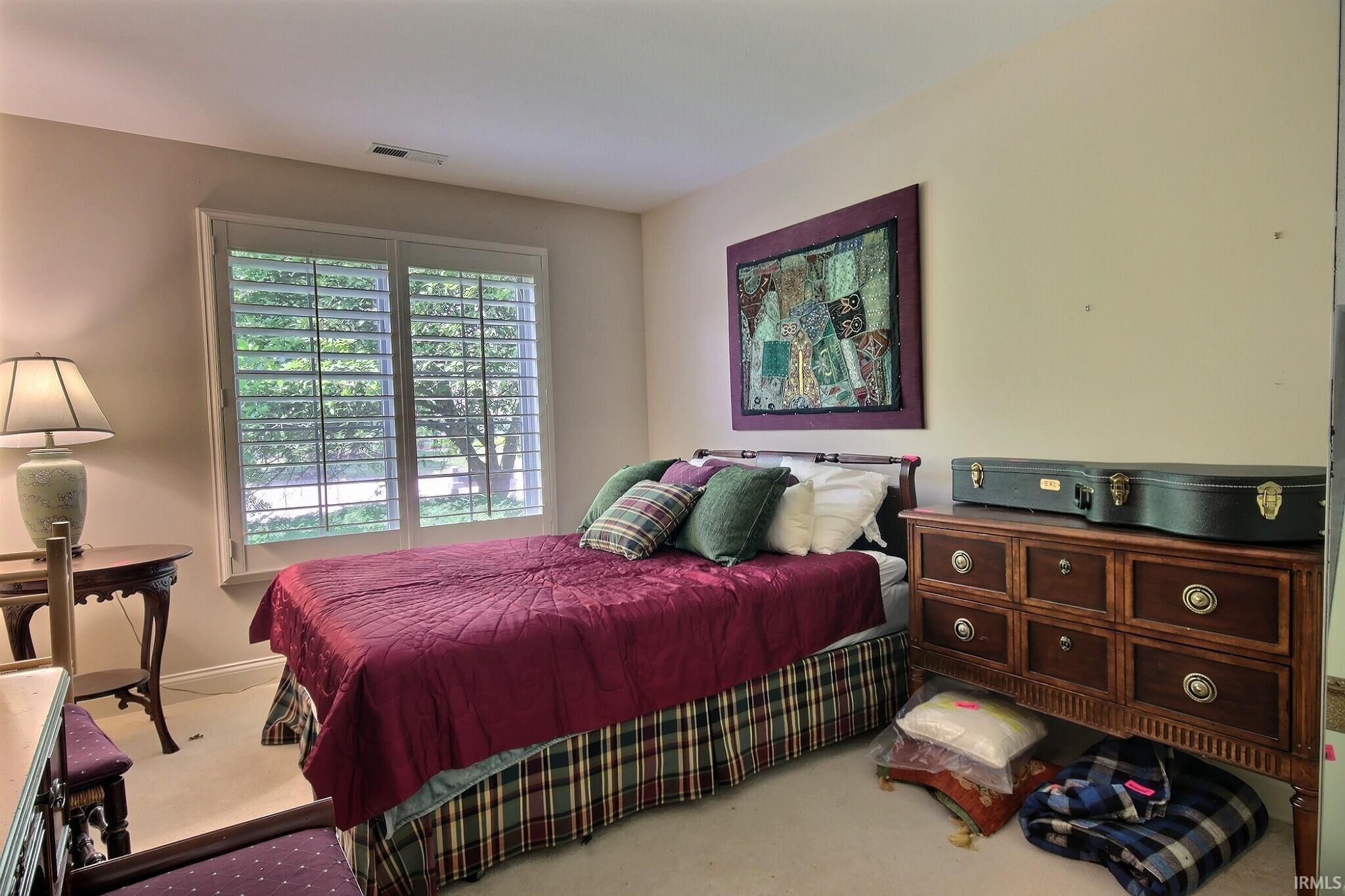 Bedroom with window featuring interior plantation shutters, light beige wall paint, and white trim