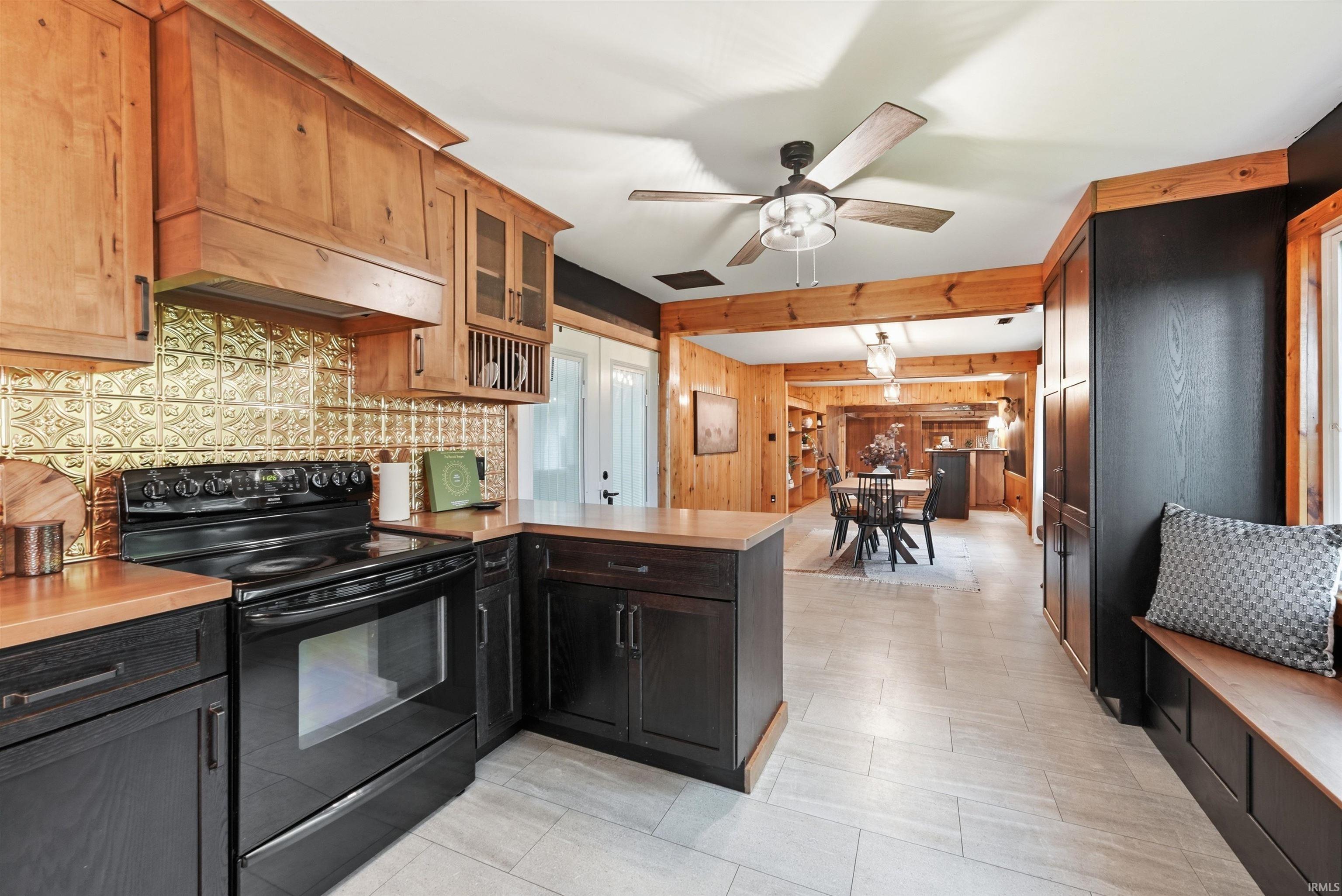 Kitchen featuring a black range, wood-finish countertops, gold-toned backsplash, light wood cabinetry, and a built-in window bench