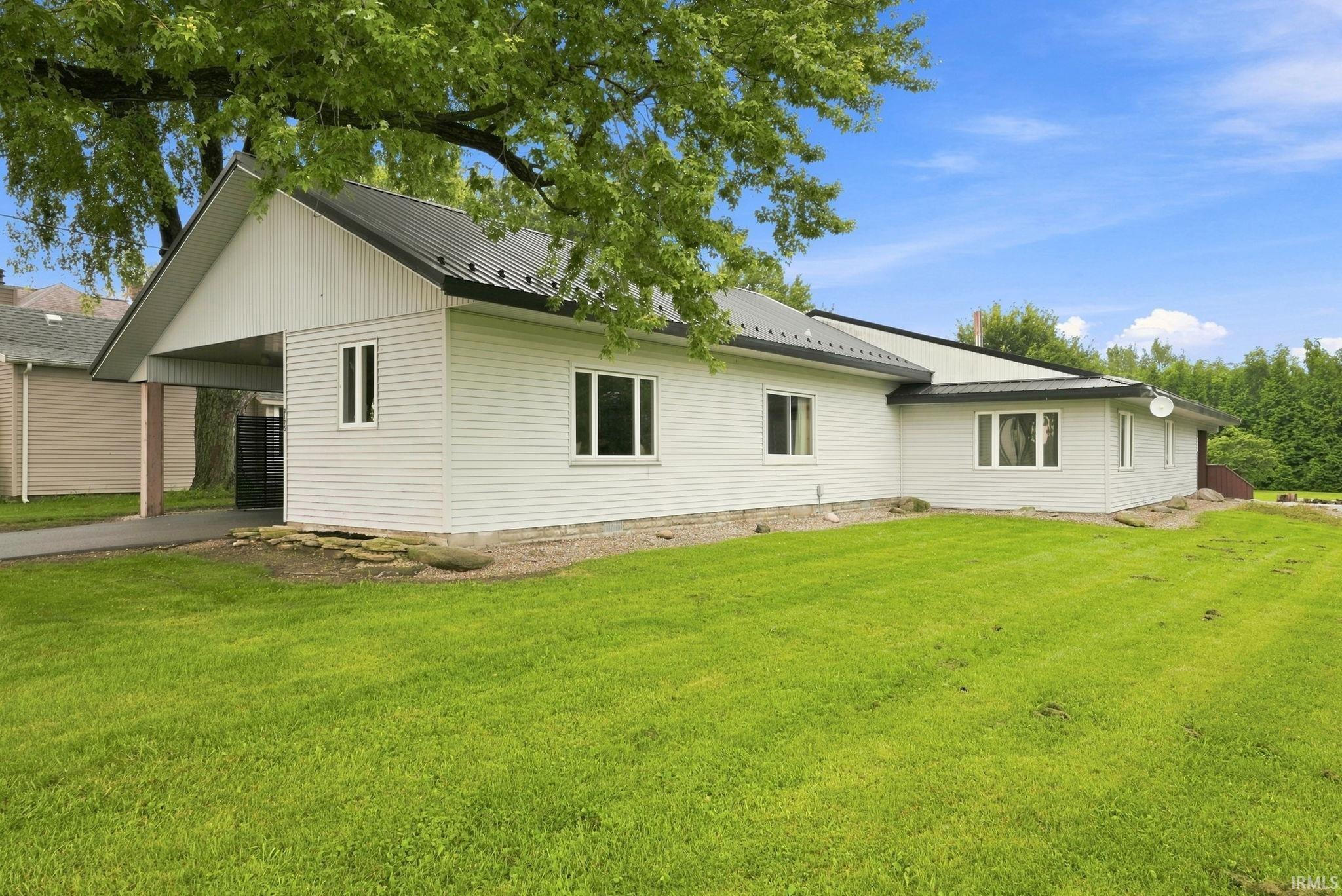White siding exterior with a dark metal roof, featuring a covered carport and multiple windows