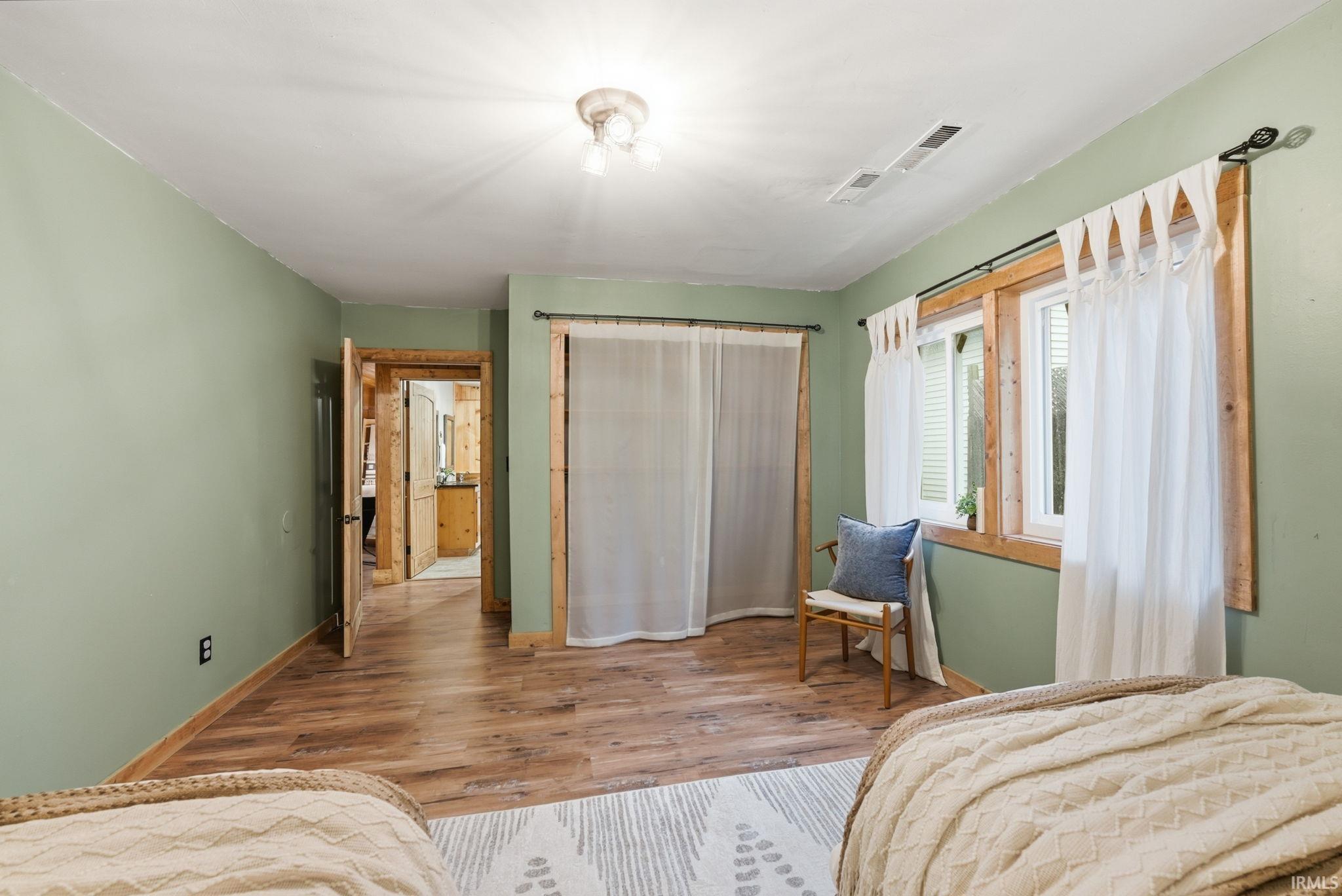 Wood-finish flooring, light green painted walls, exposed wood door frames, and a flush mount ceiling light fixture