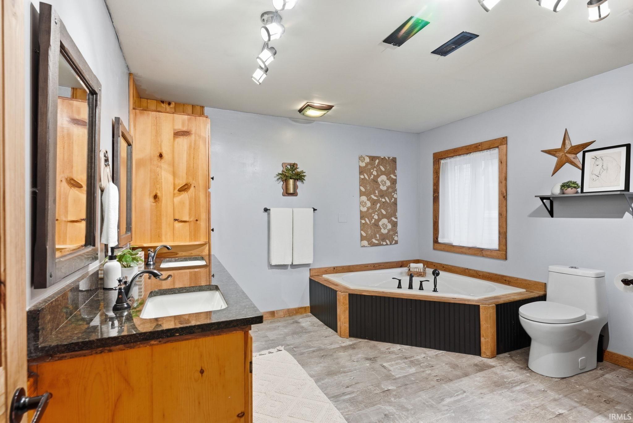 Bathroom featuring a corner soaking tub, vanity with a dark countertop, wood-finish cabinetry, and track lighting