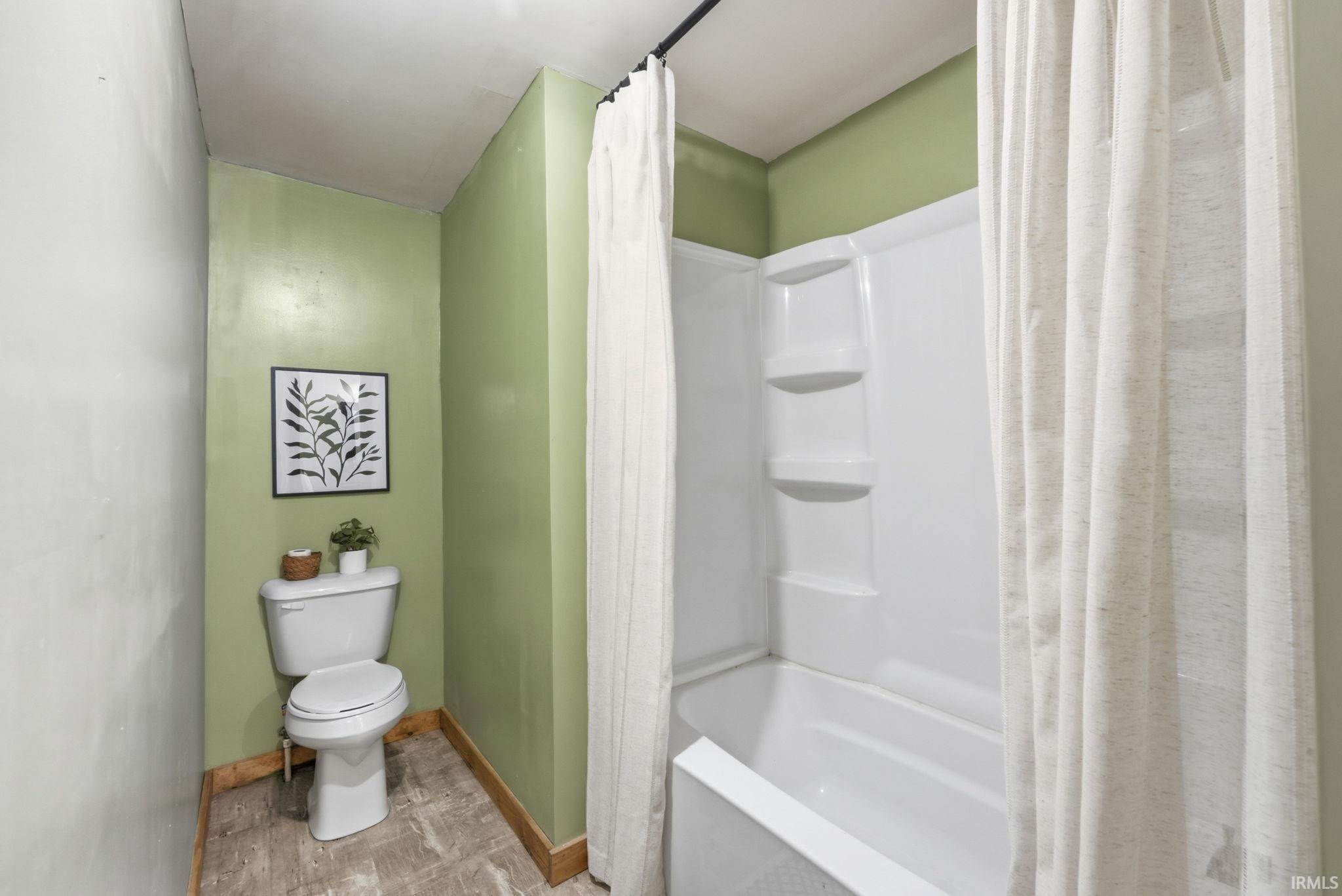 Bathtub with integrated shower, white toilet, and wood-finish flooring