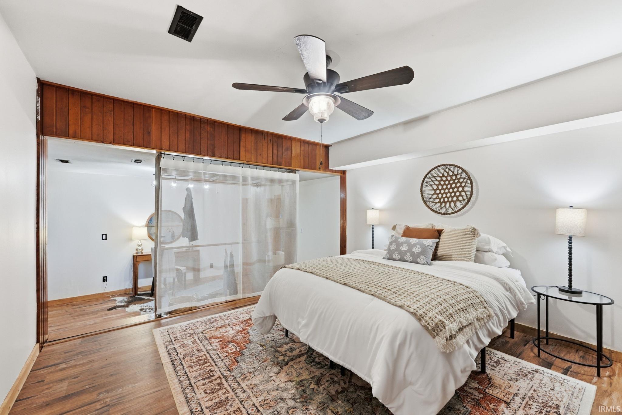 Vaulted ceiling with a ceiling fan, wood-finish flooring, and wood paneling accent