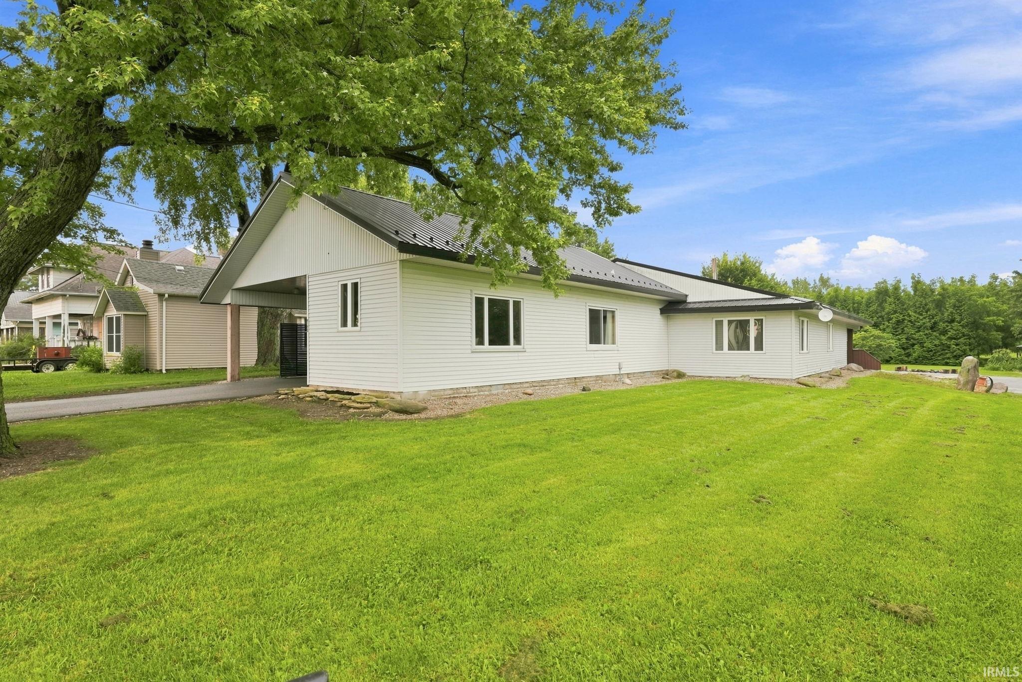 White siding exterior with a dark-pitched roof, featuring a covered entryway, multiple windows, and a large grassy yard