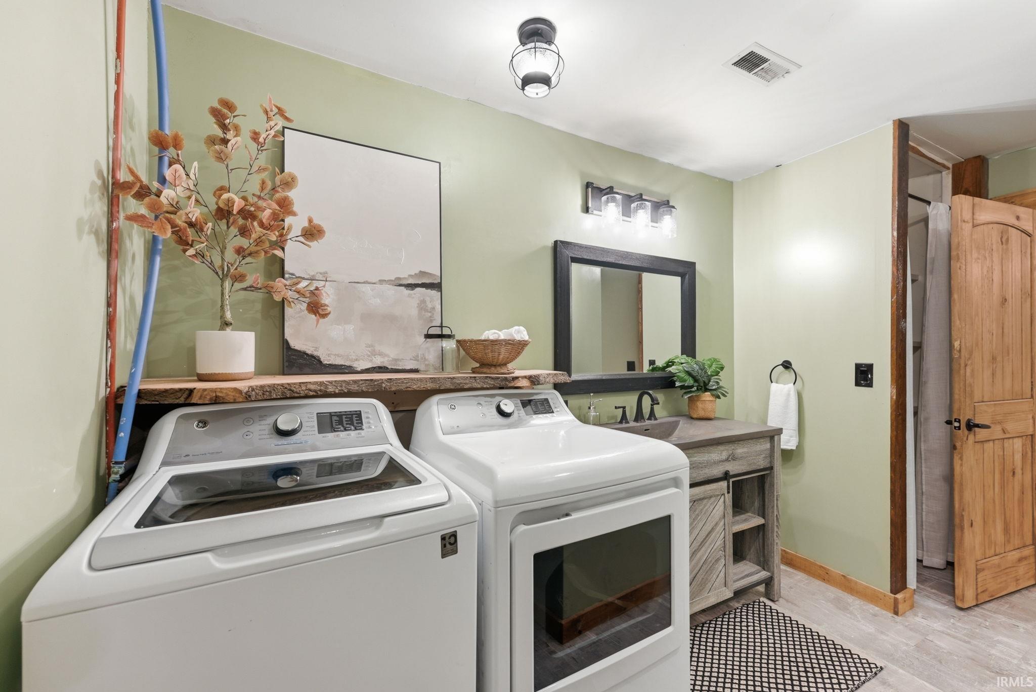 Integrated laundry appliances, live edge wood shelving, vanity with a rectangular basin sink, wood-finish flooring, and a natural wood door