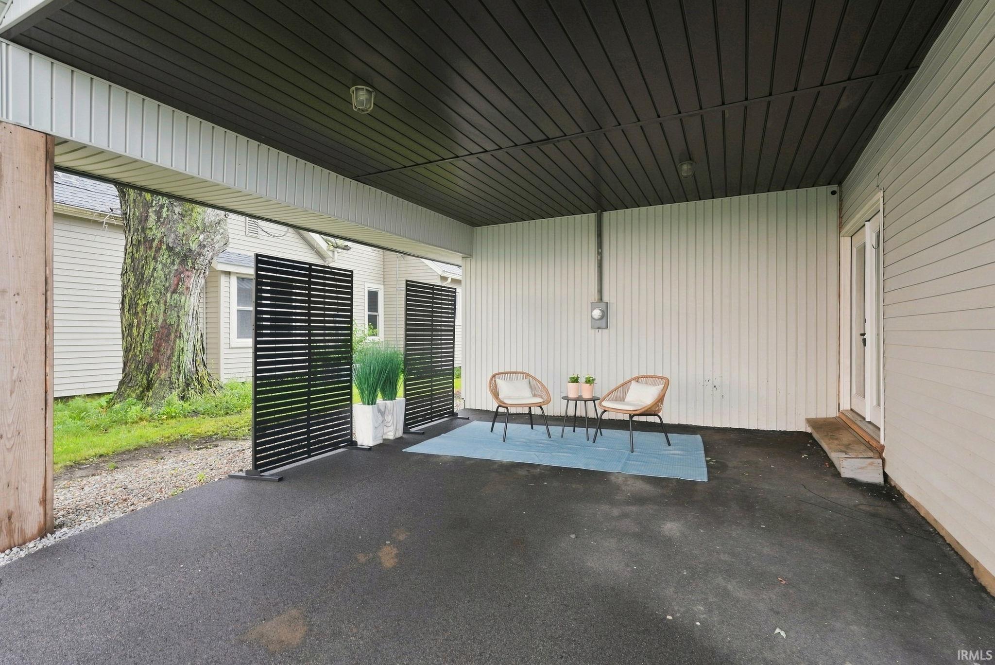 Covered patio with a dark paneled ceiling, light-toned vertical siding, and a white double door entrance