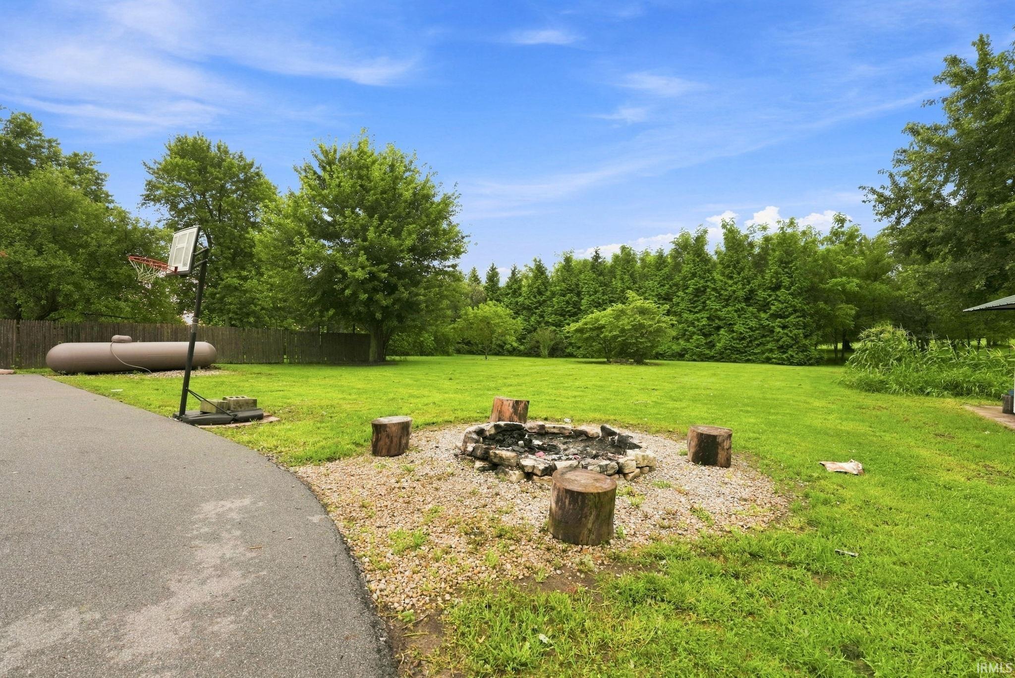 Expansive green lawn with a dedicated fire pit area, natural wood seating, and mature trees creating a private setting