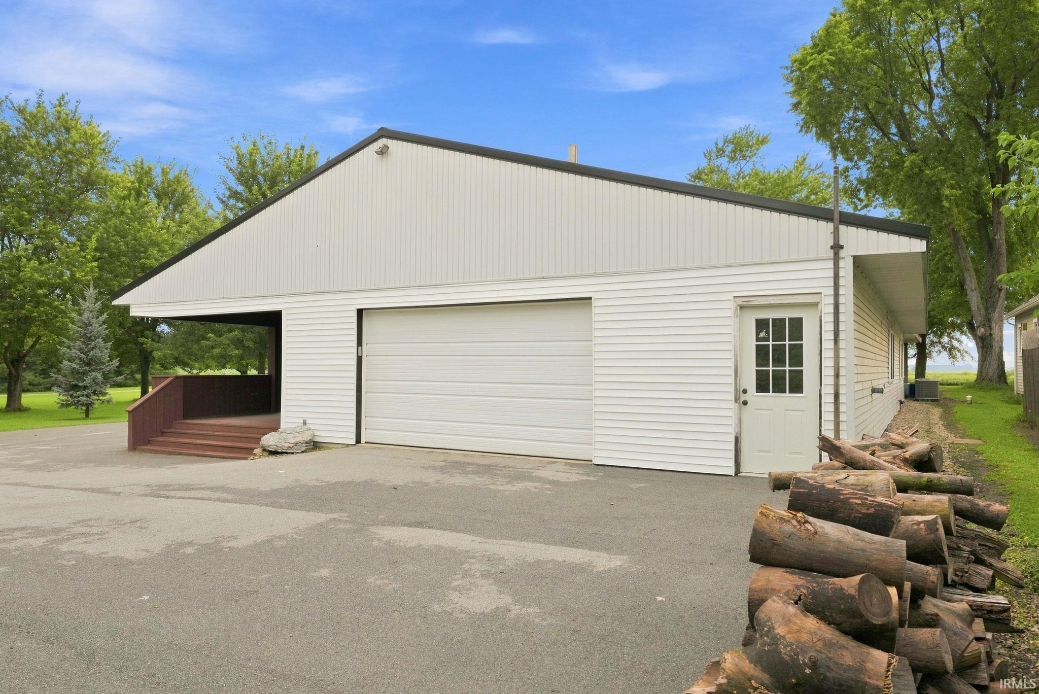 White exterior siding with a black gabled roof, a large garage door, a side entry door with windowpanes, and an attached covered patio with wood stairs