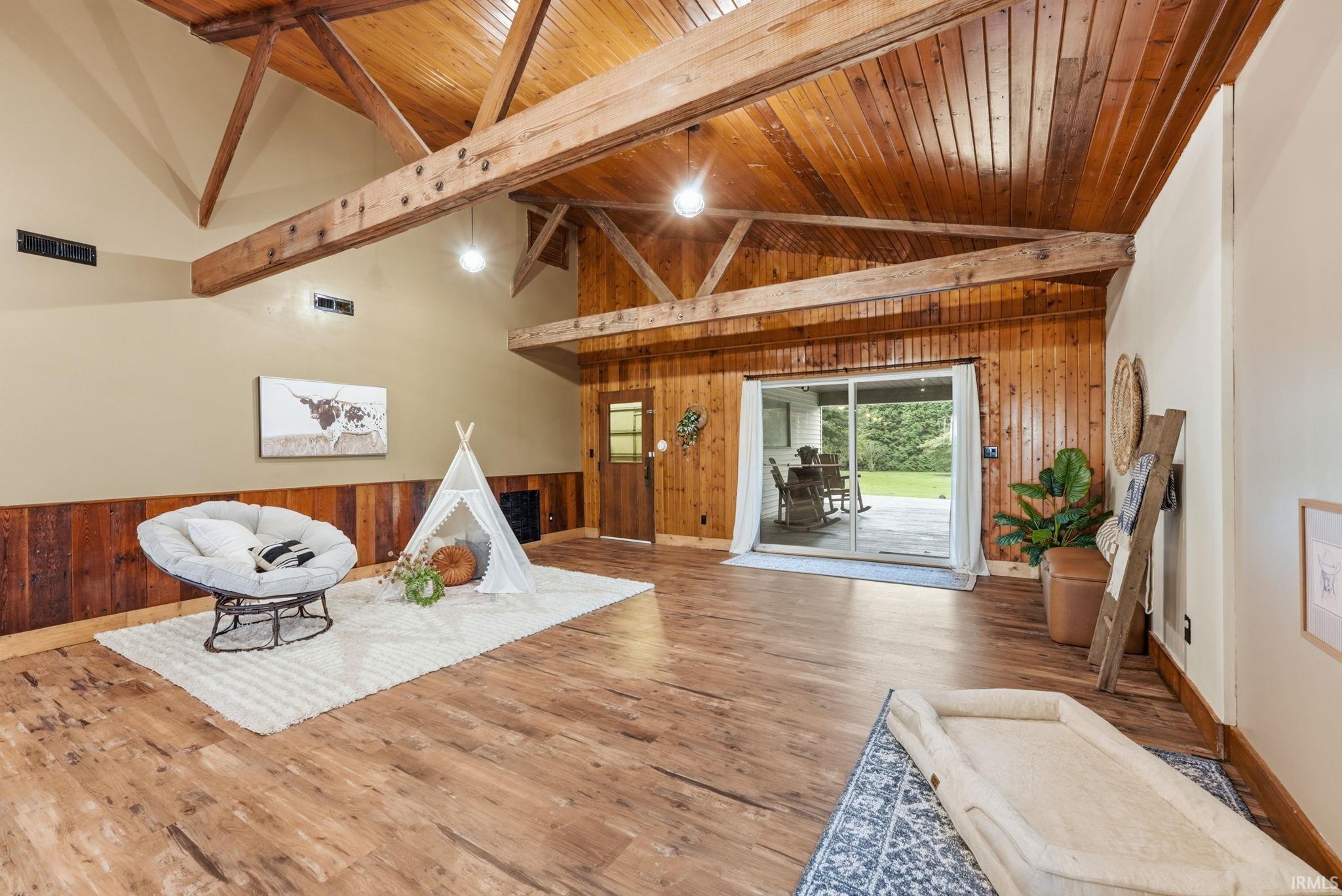Vaulted wood-paneled ceiling with exposed beams, wood-finish flooring, wood wall paneling, and sliding glass doors to the exterior