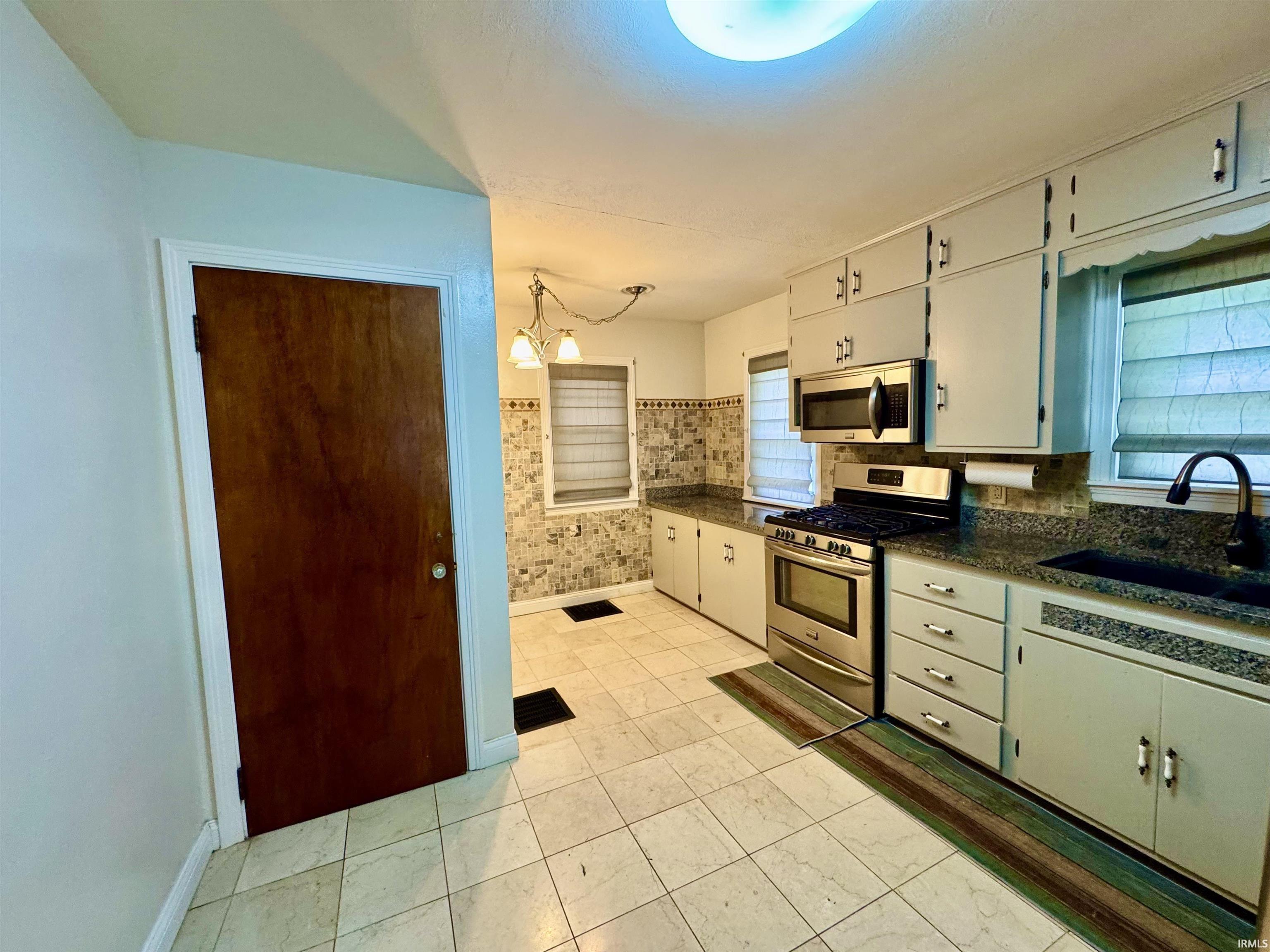 Kitchen featuring light-toned cabinetry, dark speckled countertops, and a tiled backsplash