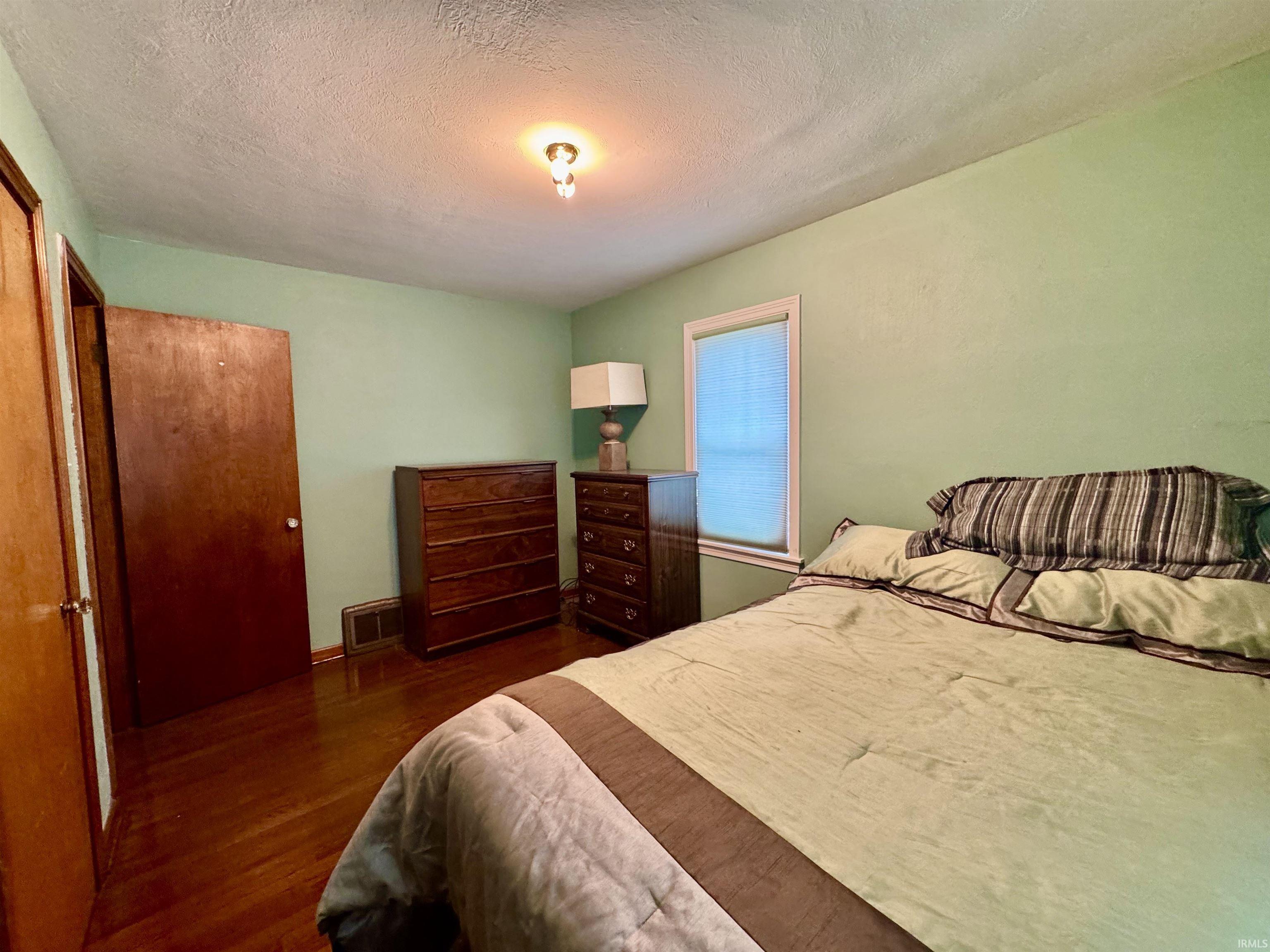 Bedroom featuring wood-finish flooring, a window with blinds, and a built-in closet with a wood door