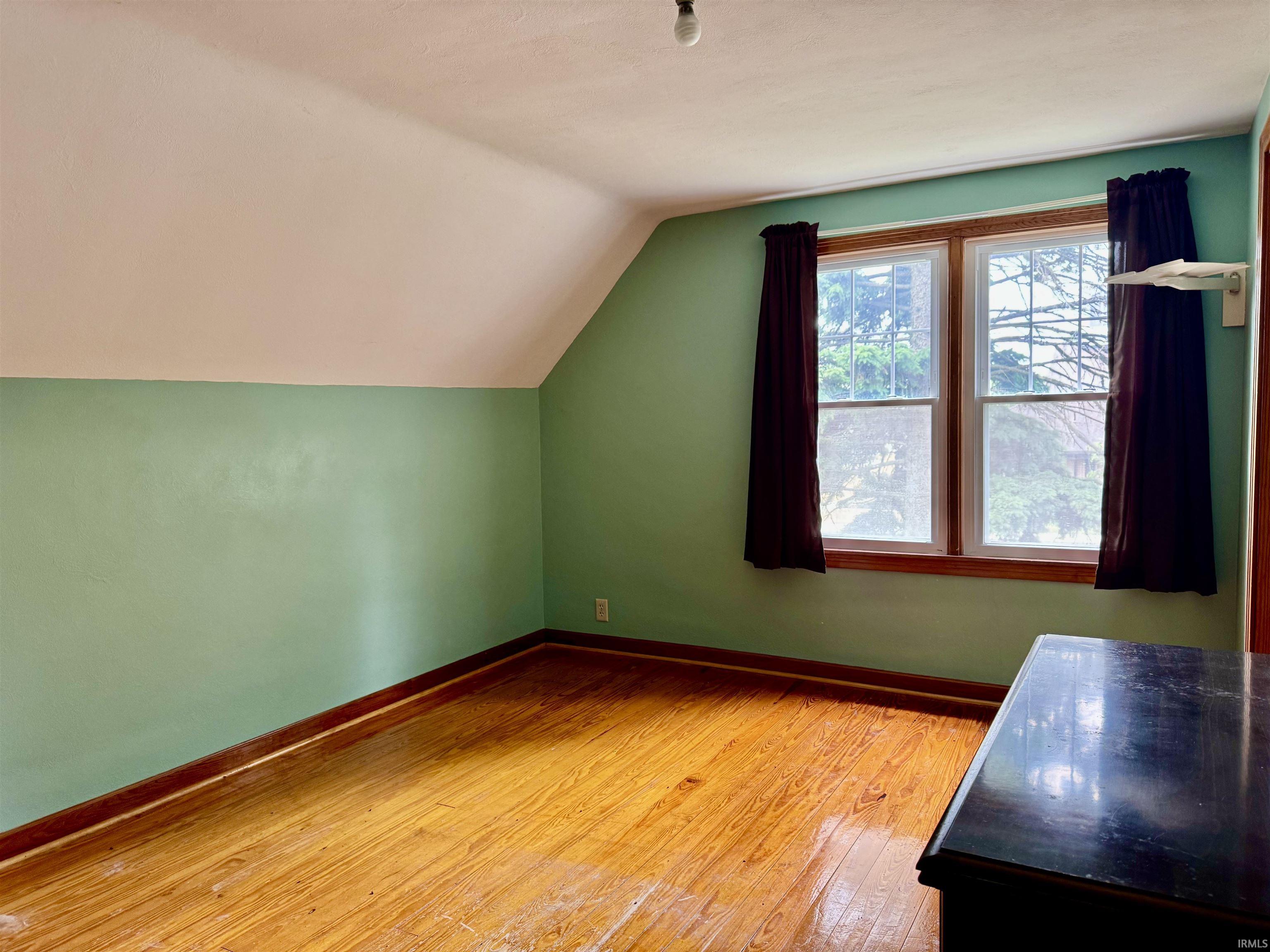 Room featuring wood-finish flooring, a pitched ceiling, and dual windows with wood trim
