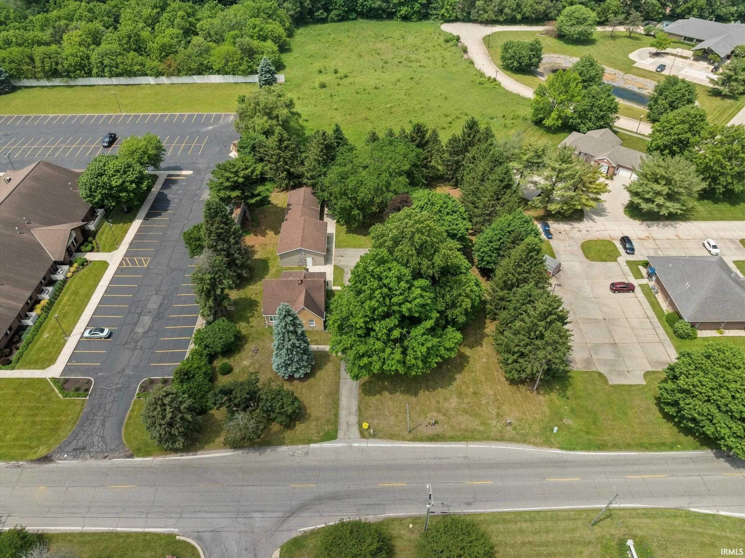 Aerial overview of a property featuring mature trees and a prominent roadside location