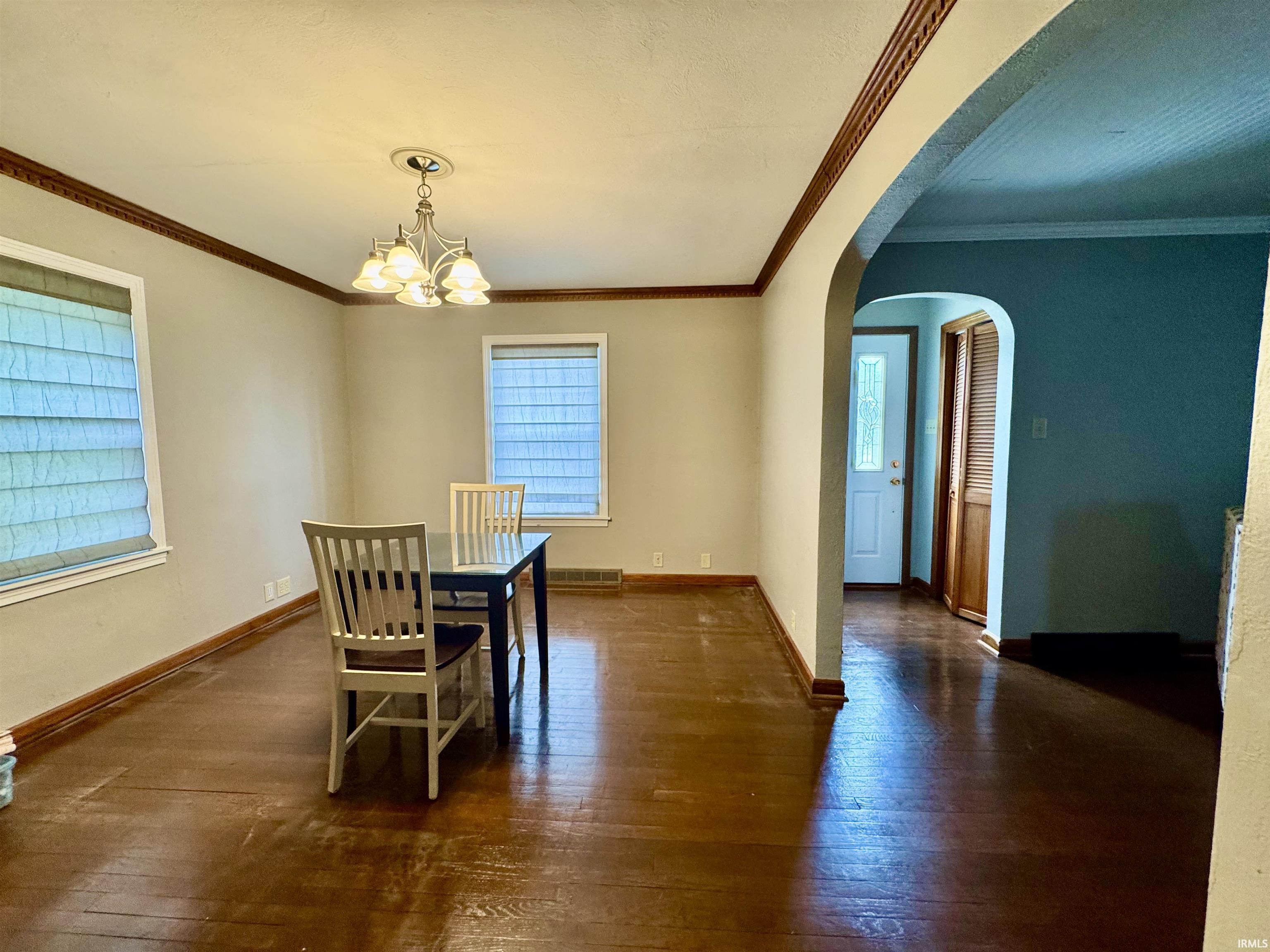 Spacious room featuring wood-finish flooring, decorative ceiling trim, and a chandelier with a ceiling medallion