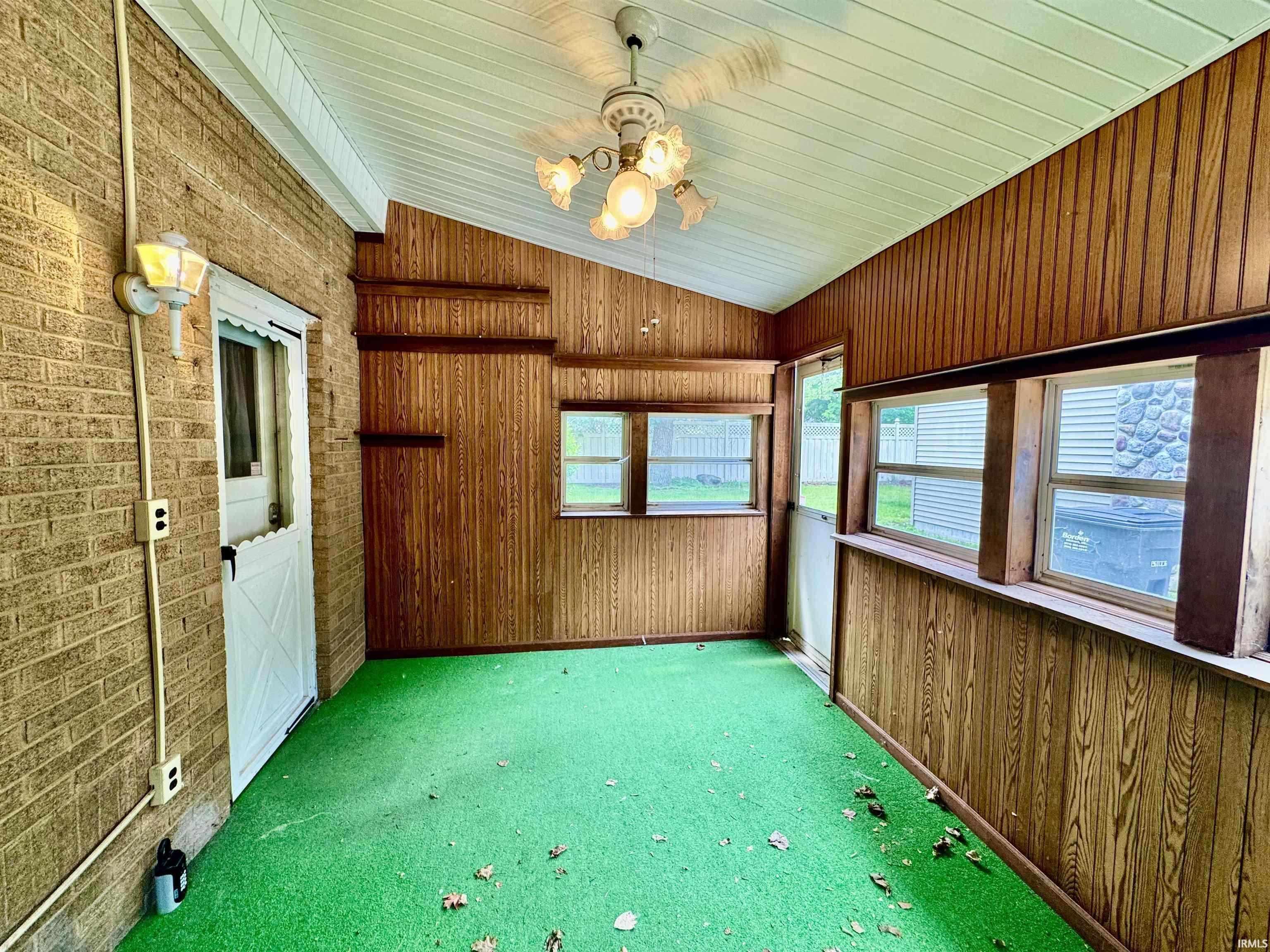 Enclosed porch featuring a brick wall, wood paneling, multiple windows, a ceiling fan with light fixture, and a white Dutch door