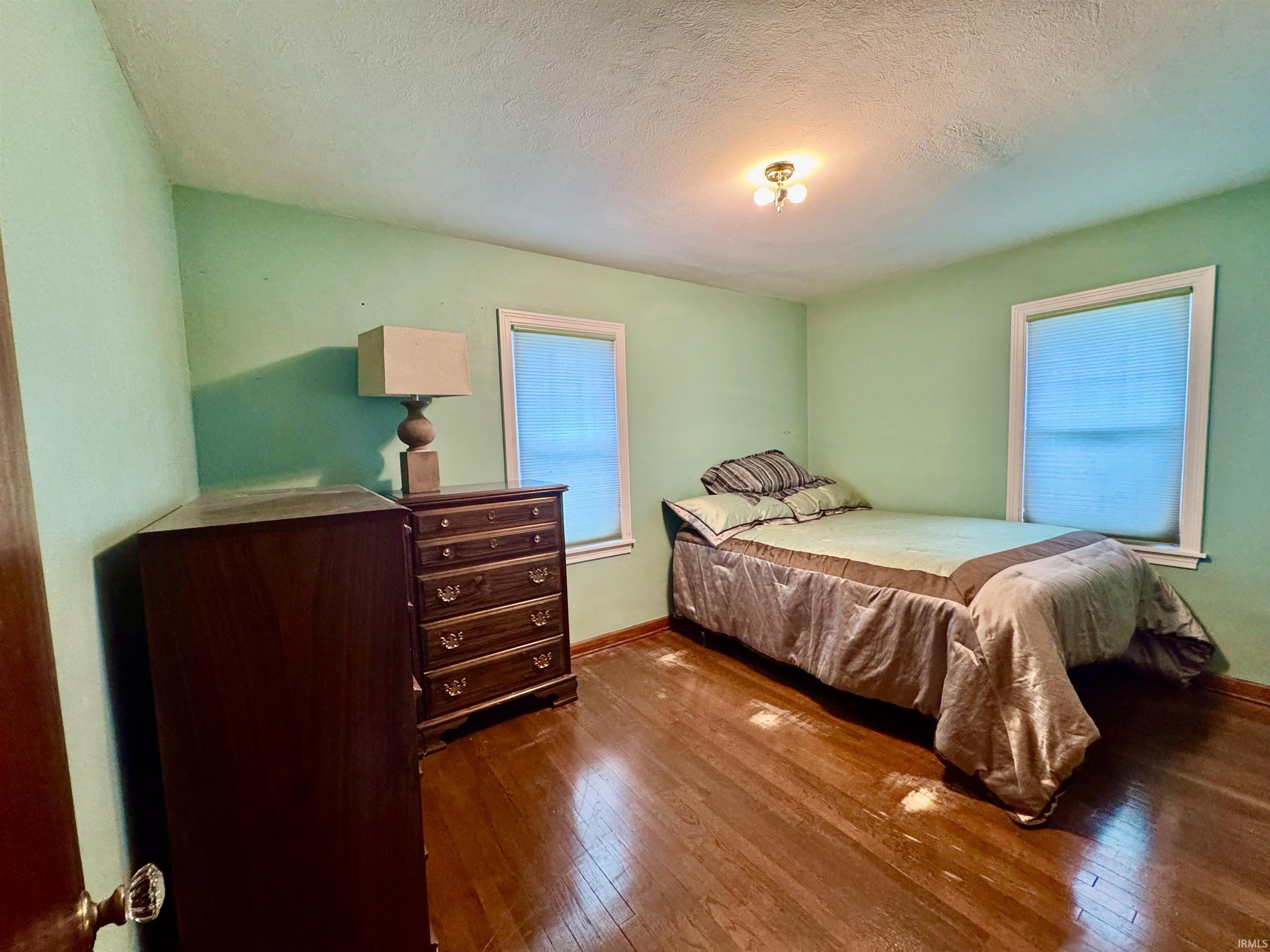 Room featuring wood-finish flooring and two windows with blinds
