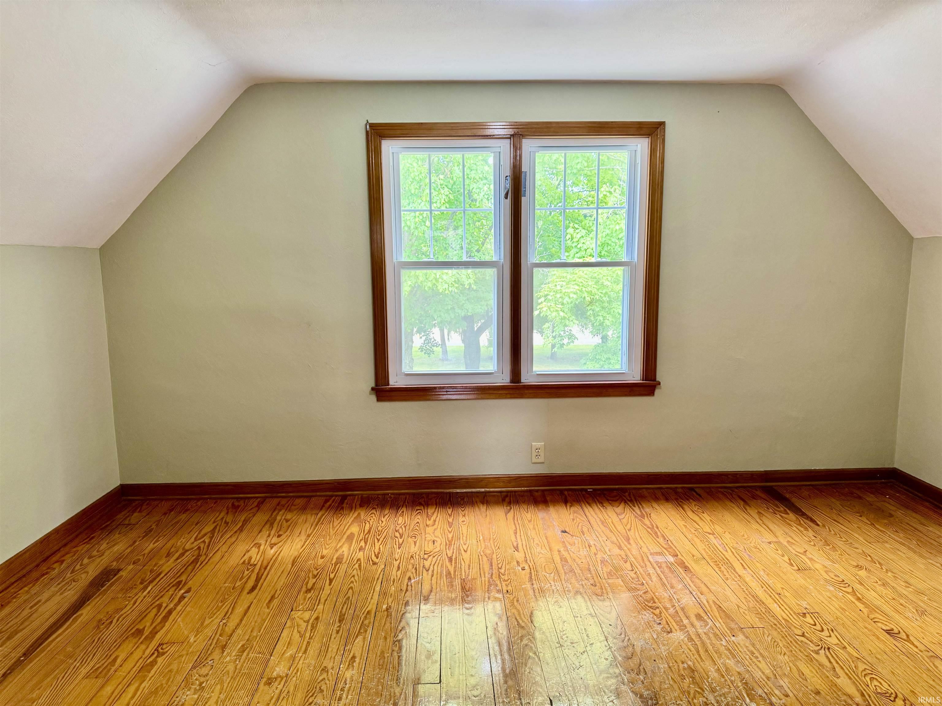 Room featuring sloped ceilings, wood-finish flooring, and a double window with wood trim
