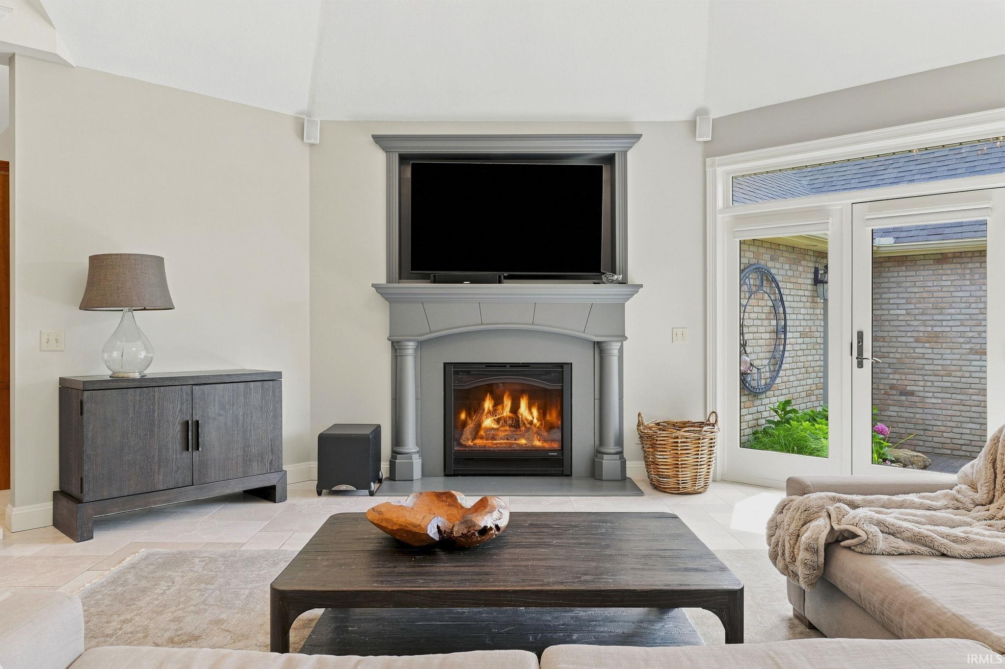 Vaulted great room featuring heated floors, abundant natural light, courtyard views, and a stunning fireplace.