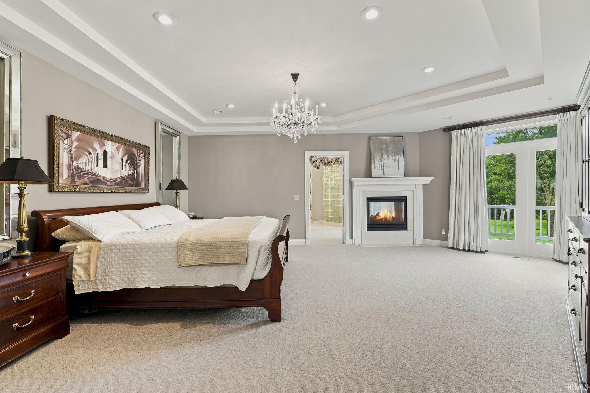 Expansive primary suite featuring a tray ceiling, private balcony access, and a double-sided fireplace.