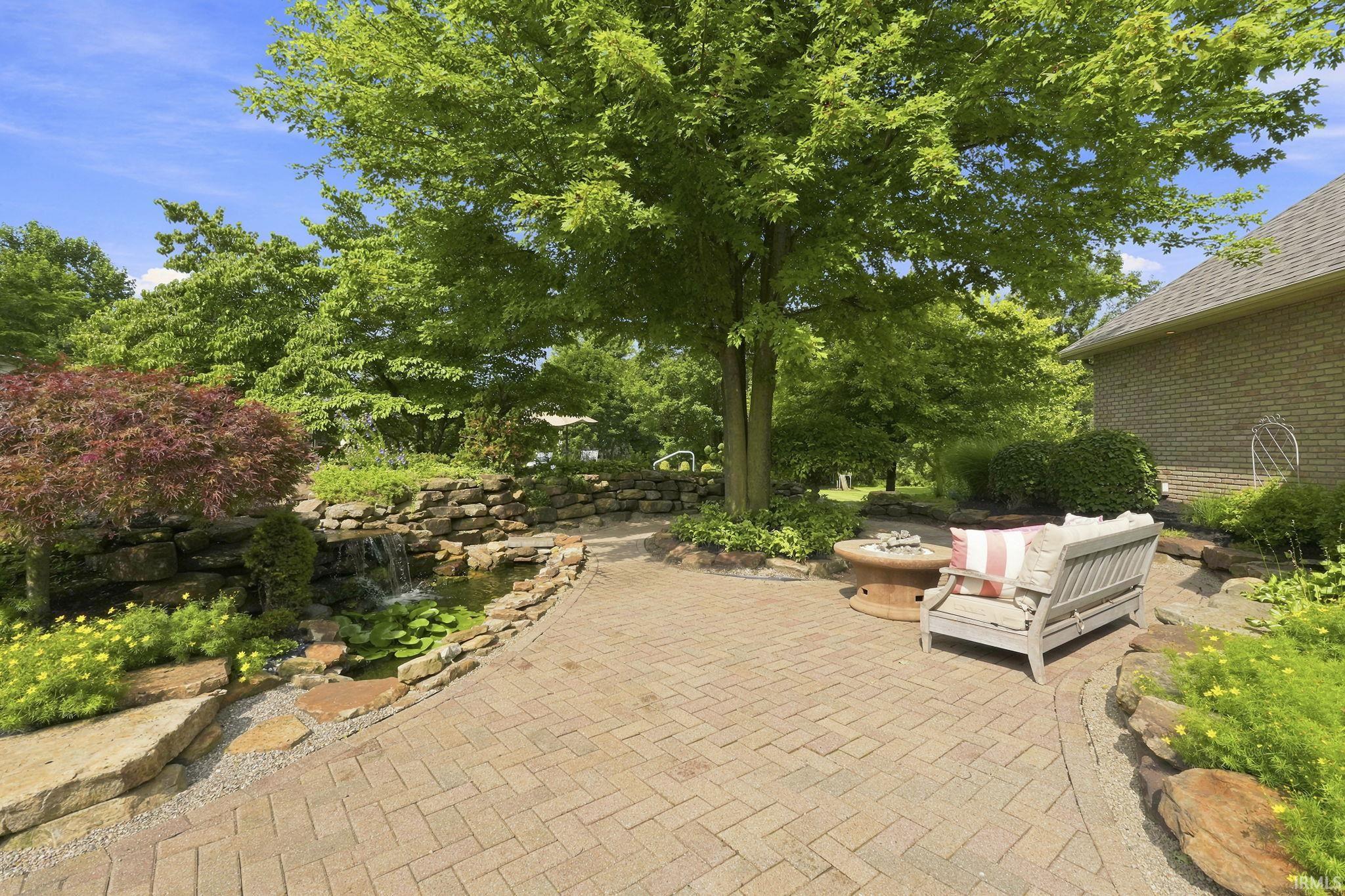 Private paver patio off the great room featuring a tranquil waterfall, mature shade tree, and serene outdoor retreat.