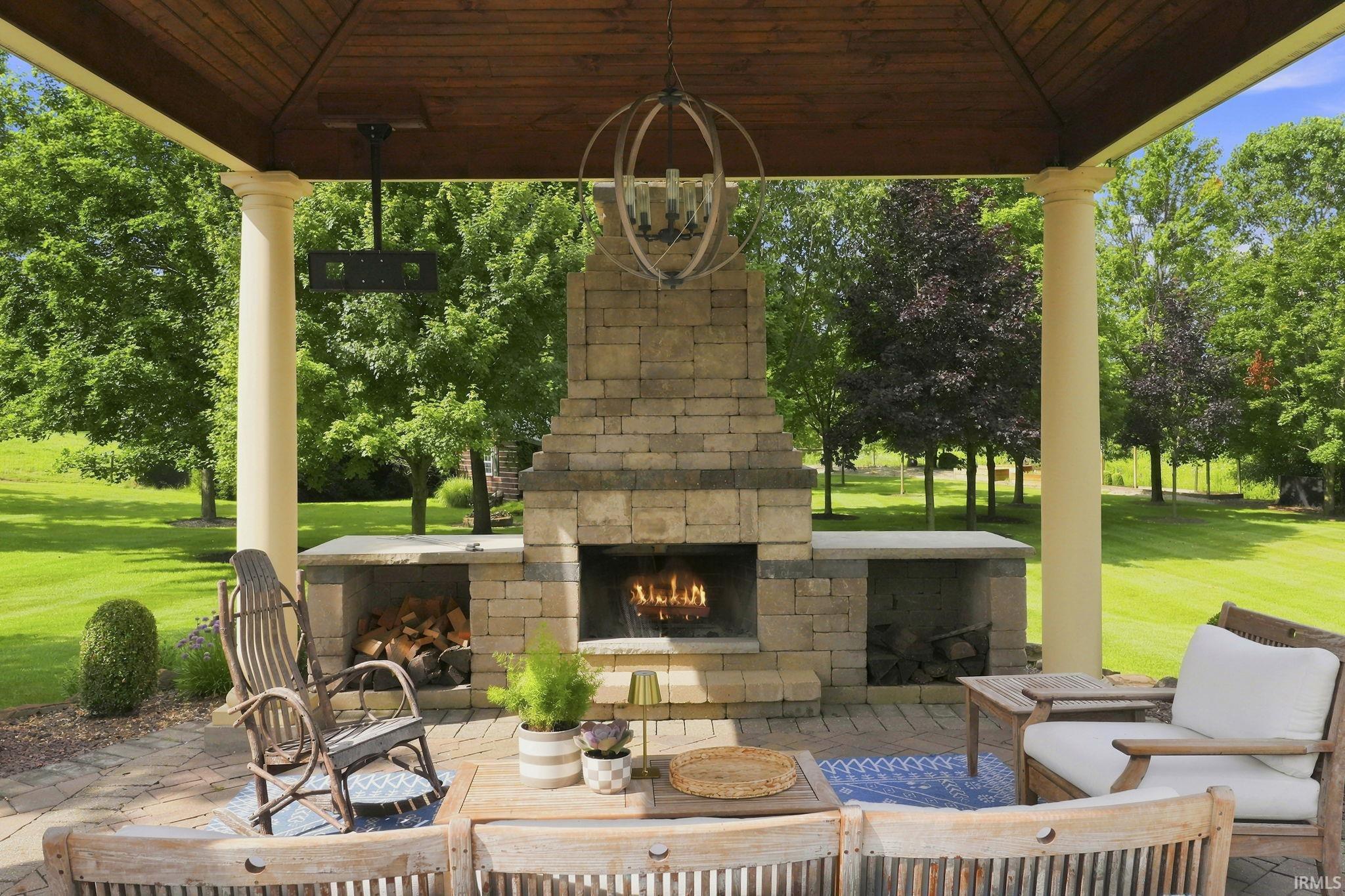 Covered outdoor living space featuring stately columns, masonry fireplace, and relaxing views of the pool with space for entertaining or outdoor TV enjoyment.