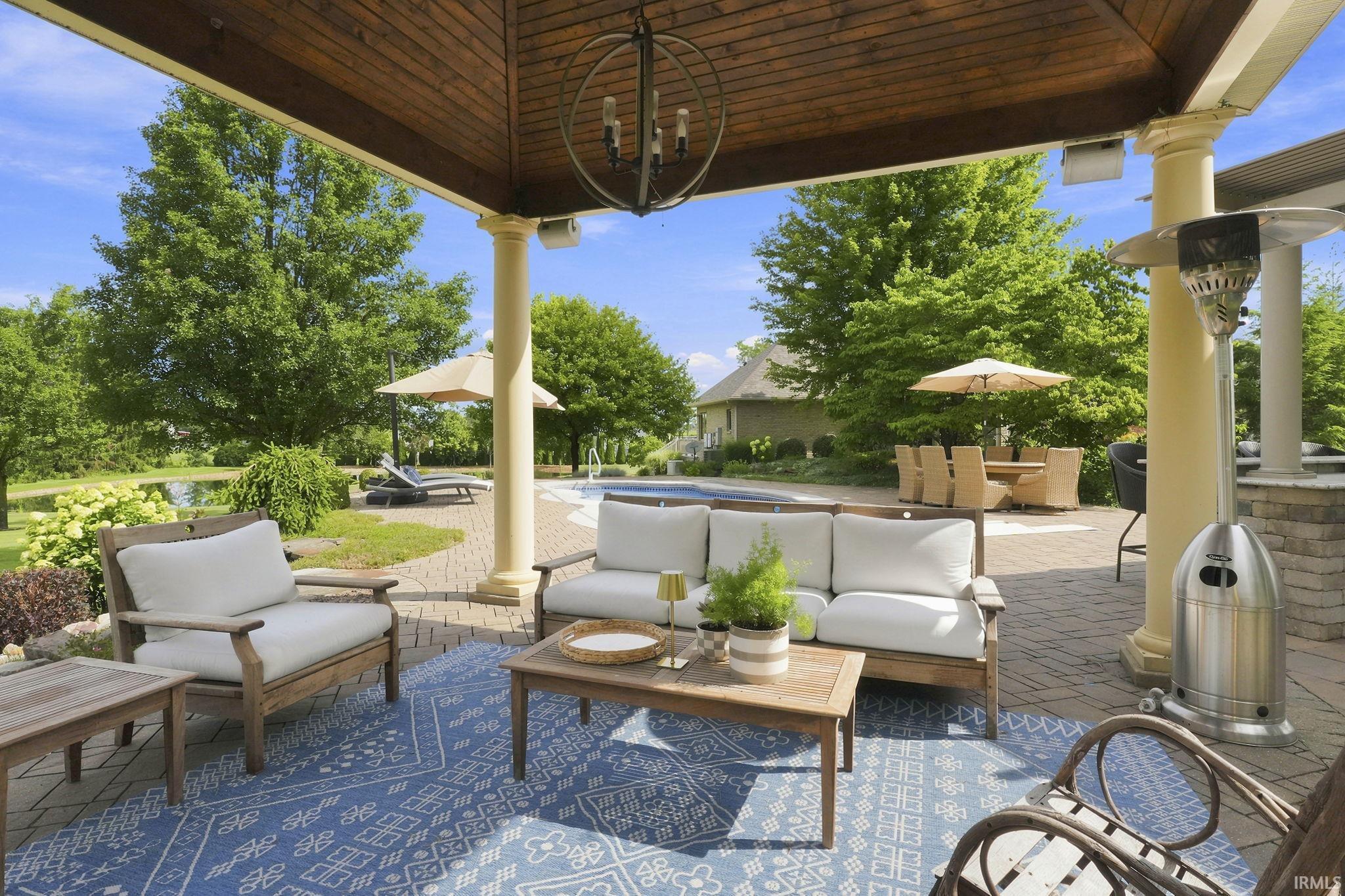 Covered outdoor living space featuring stately columns, masonry fireplace, and relaxing views of the pool with space for entertaining or outdoor TV enjoyment.