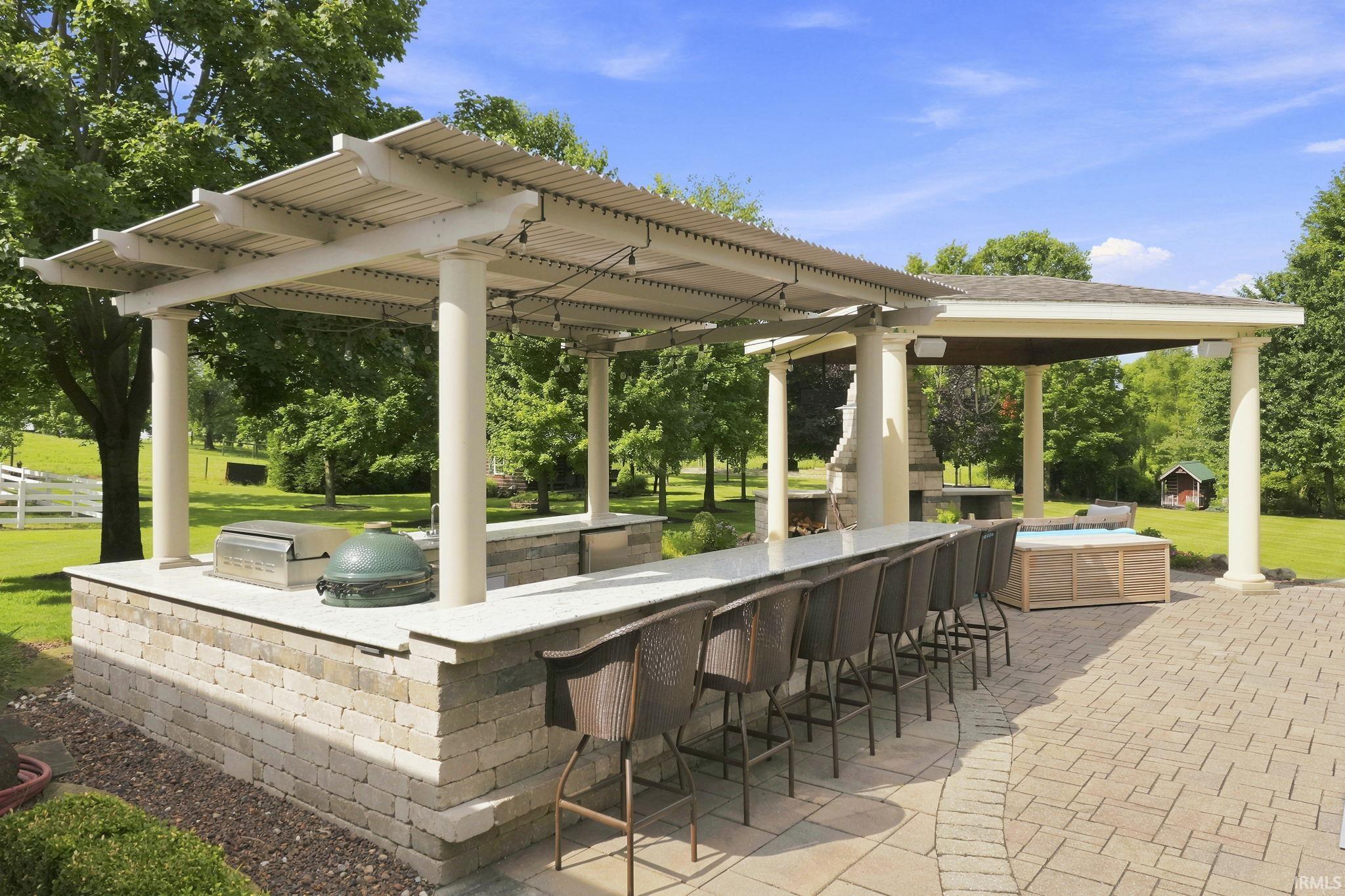 Outdoor kitchen featuring a smart pergola, built-in grill, Green Egg, dual burners, refrigerator, sink, ample storage, and generous serving space with bar seating.
