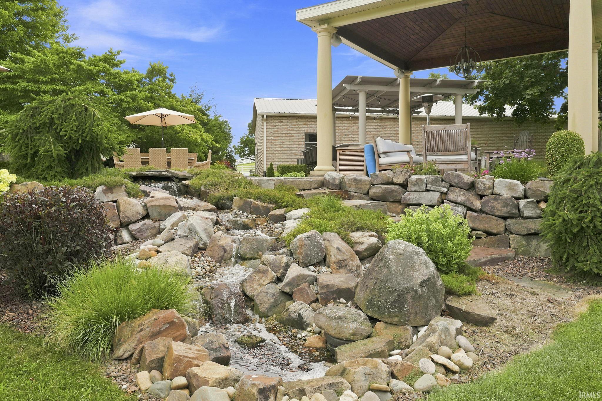 Beautifully landscaped pathway leading from the pool terrace to the backyard, featuring cascading waterfall features and serene natural surroundings.