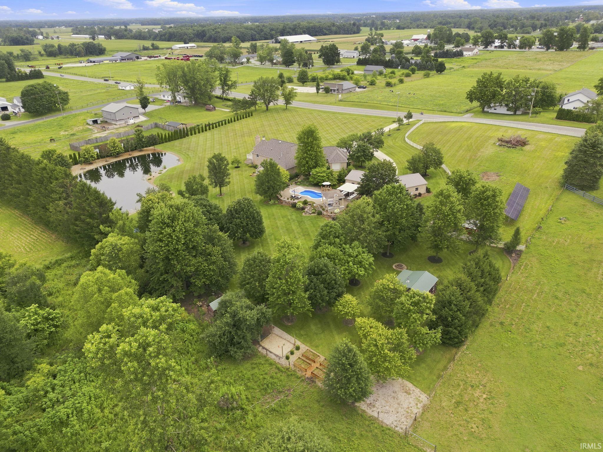 Aerial view capturing the full beauty and scale of this private estate, showcasing the custom home, pond, pool, outdoor living spaces, workshop, and expansive acreage surrounded by peaceful countryside.