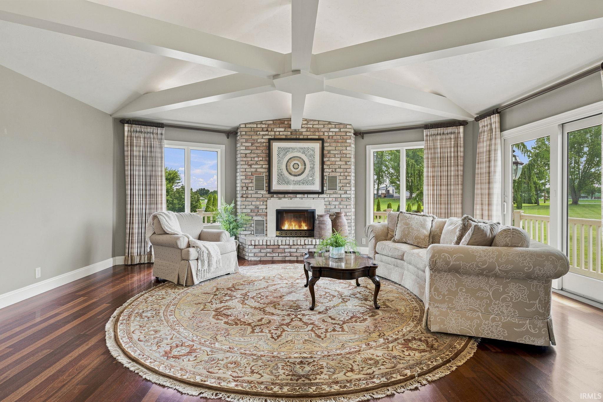 Octagonal formal living room featuring a vaulted beam ceiling, fireplace, and panoramic pond views.