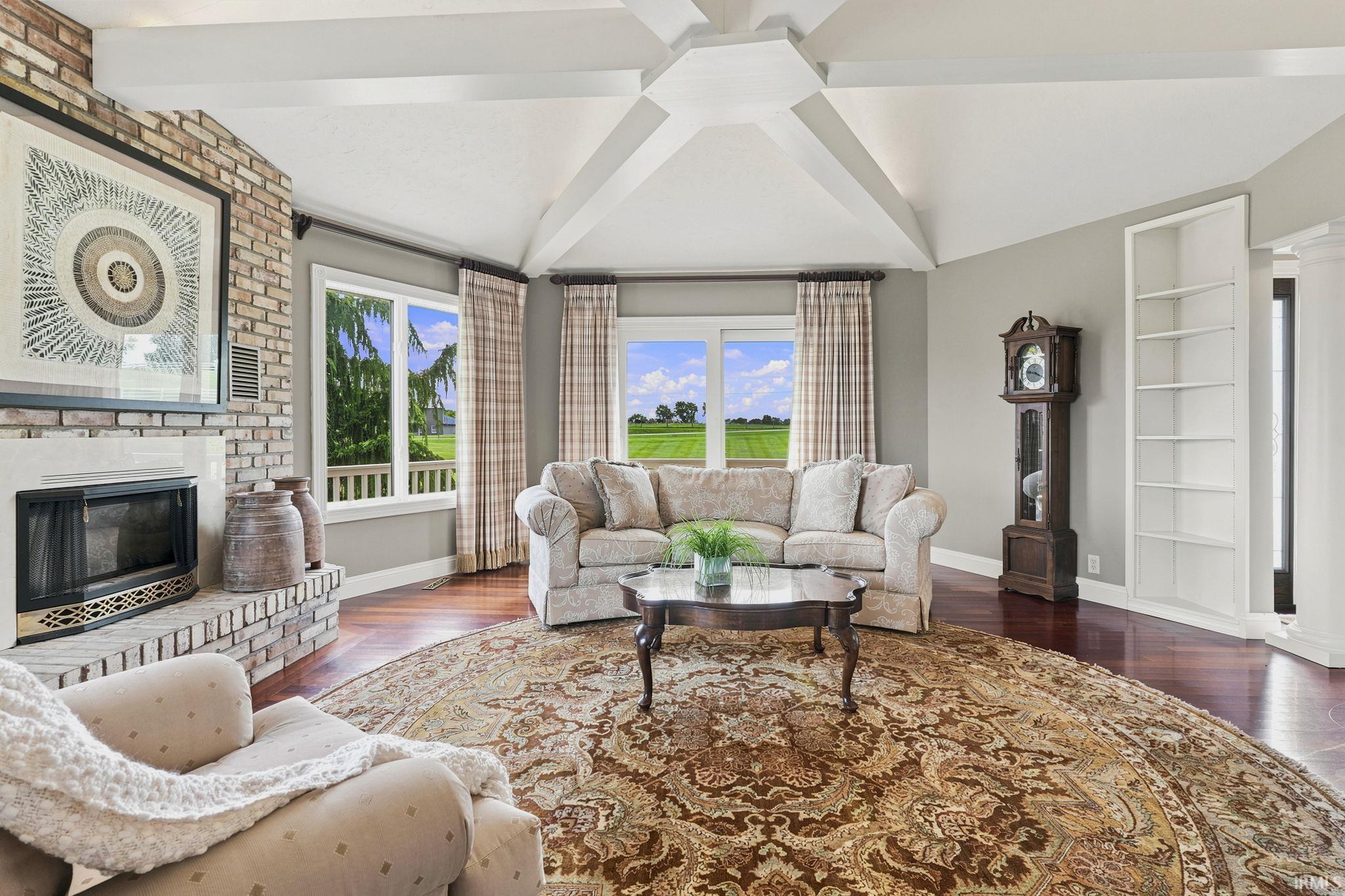 Octagonal formal living room featuring a vaulted beam ceiling, fireplace, and panoramic pond views.