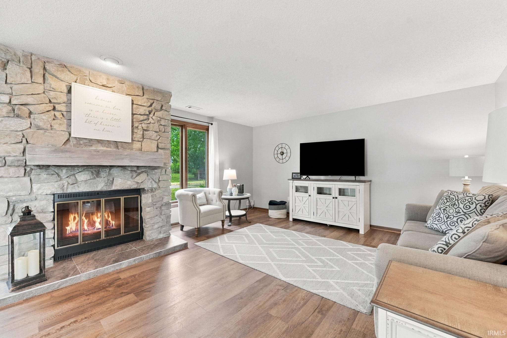 Living area featuring a stone-clad fireplace with hearth, wood-finish flooring, a large window, and recessed lighting