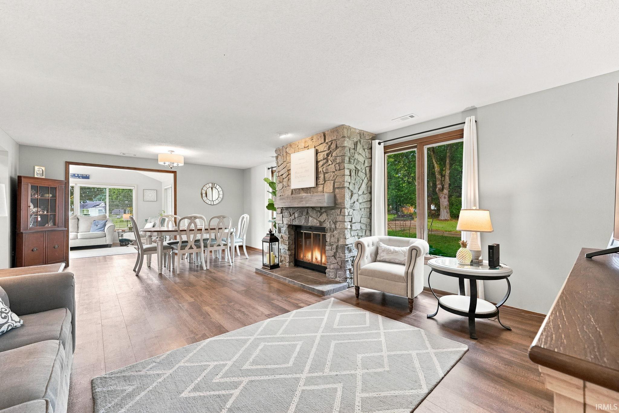 Spacious living area featuring wood-finish flooring, a stone-clad fireplace, and large windows