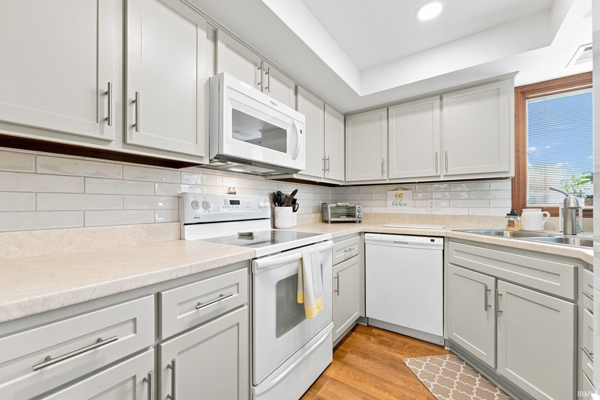 Kitchen featuring light gray cabinetry with brushed nickel hardware, white subway tile backsplash, and a corner sink with a stainless steel faucet
