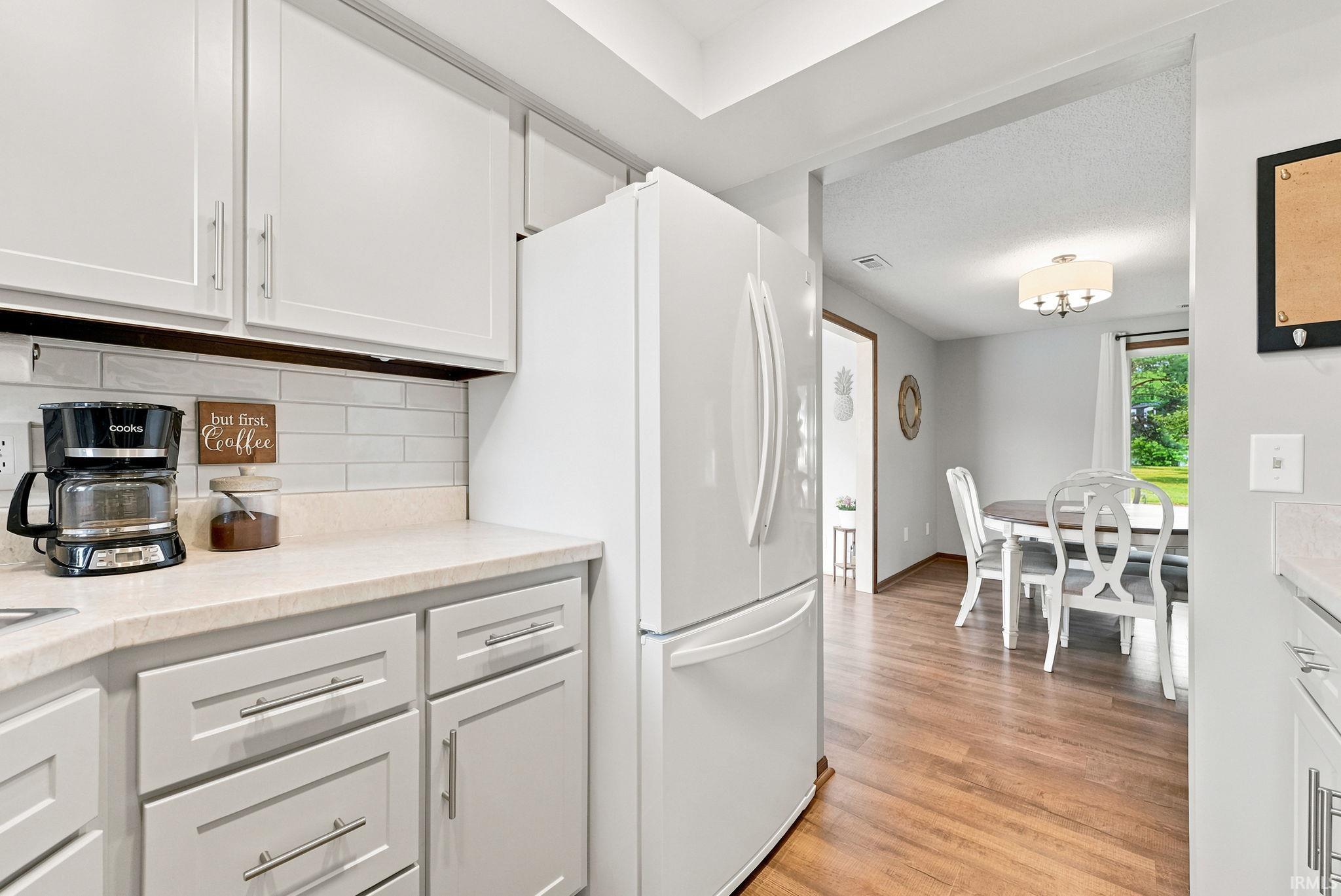 Kitchen featuring white cabinetry, light-toned countertops, a subway tile backsplash, and a white refrigerator