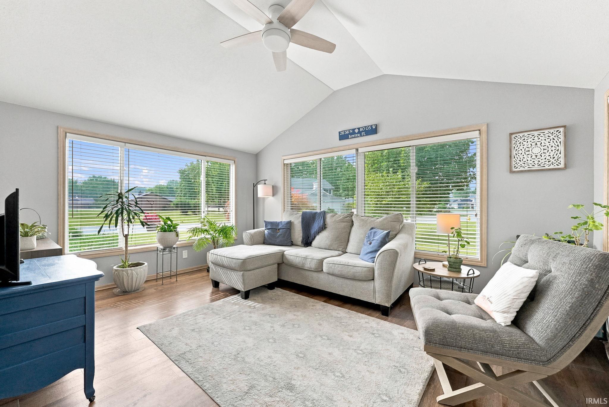 Vaulted ceiling living area featuring wood-finish flooring, a contemporary ceiling fan, and large windows with horizontal blinds