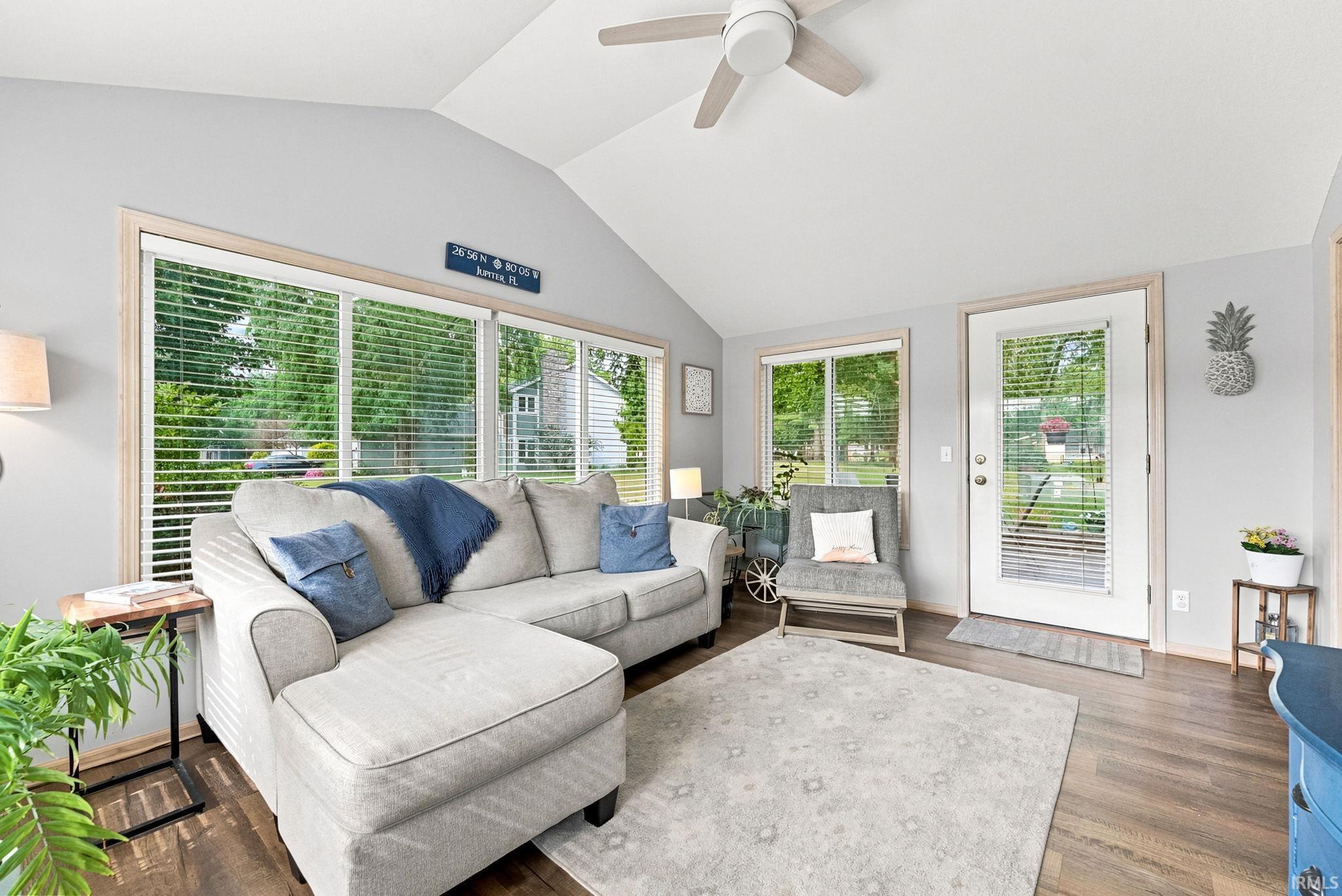 Vaulted ceiling living space featuring wood-finish flooring, a white ceiling fan, and large windows with blinds