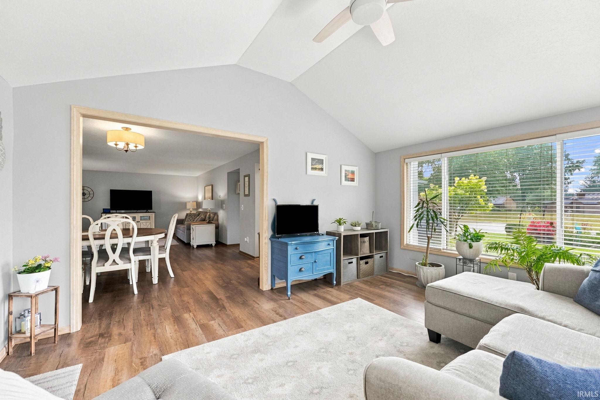 Vaulted ceilings featuring a ceiling fan, wood-finish flooring, and a large picture window with blinds