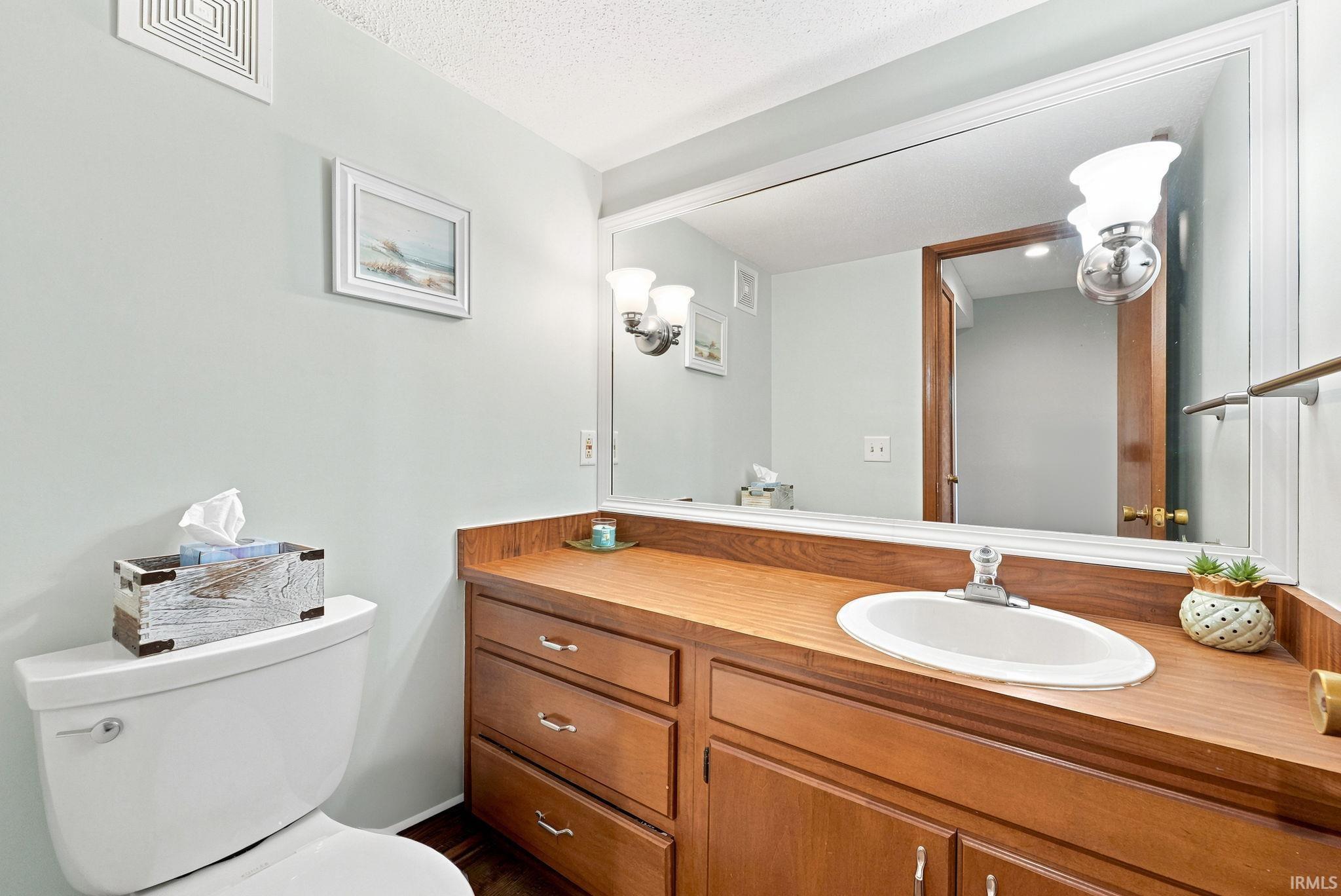 Bathroom featuring a wood-finish vanity with an integrated sink, a large wall-mounted mirror, and overhead sconce lighting