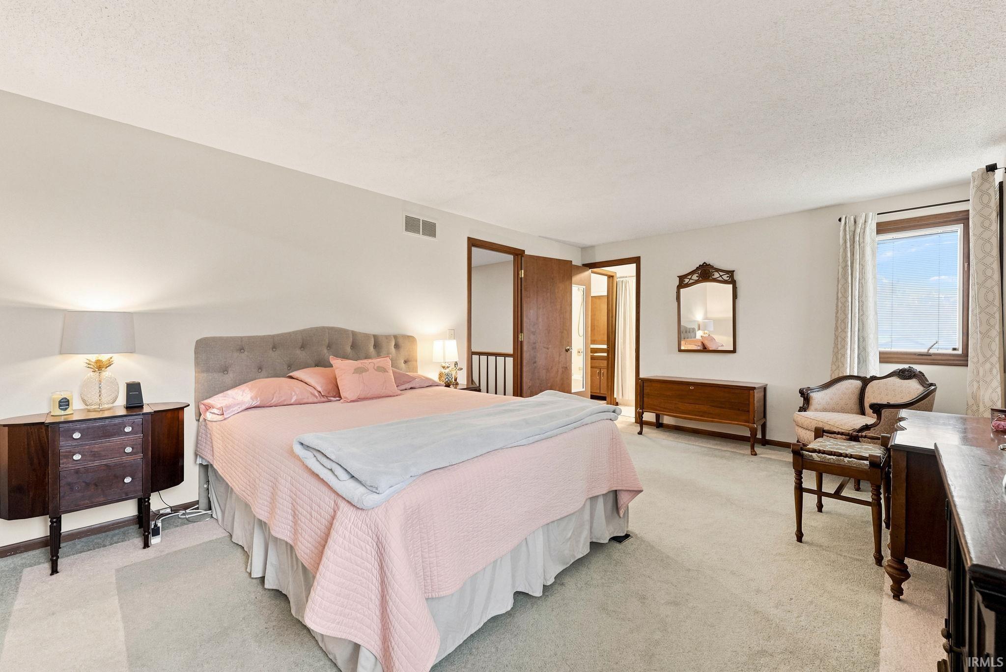 Spacious bedroom featuring light-toned carpeting, a window with natural light, a wood-paneled door, and ample wall space