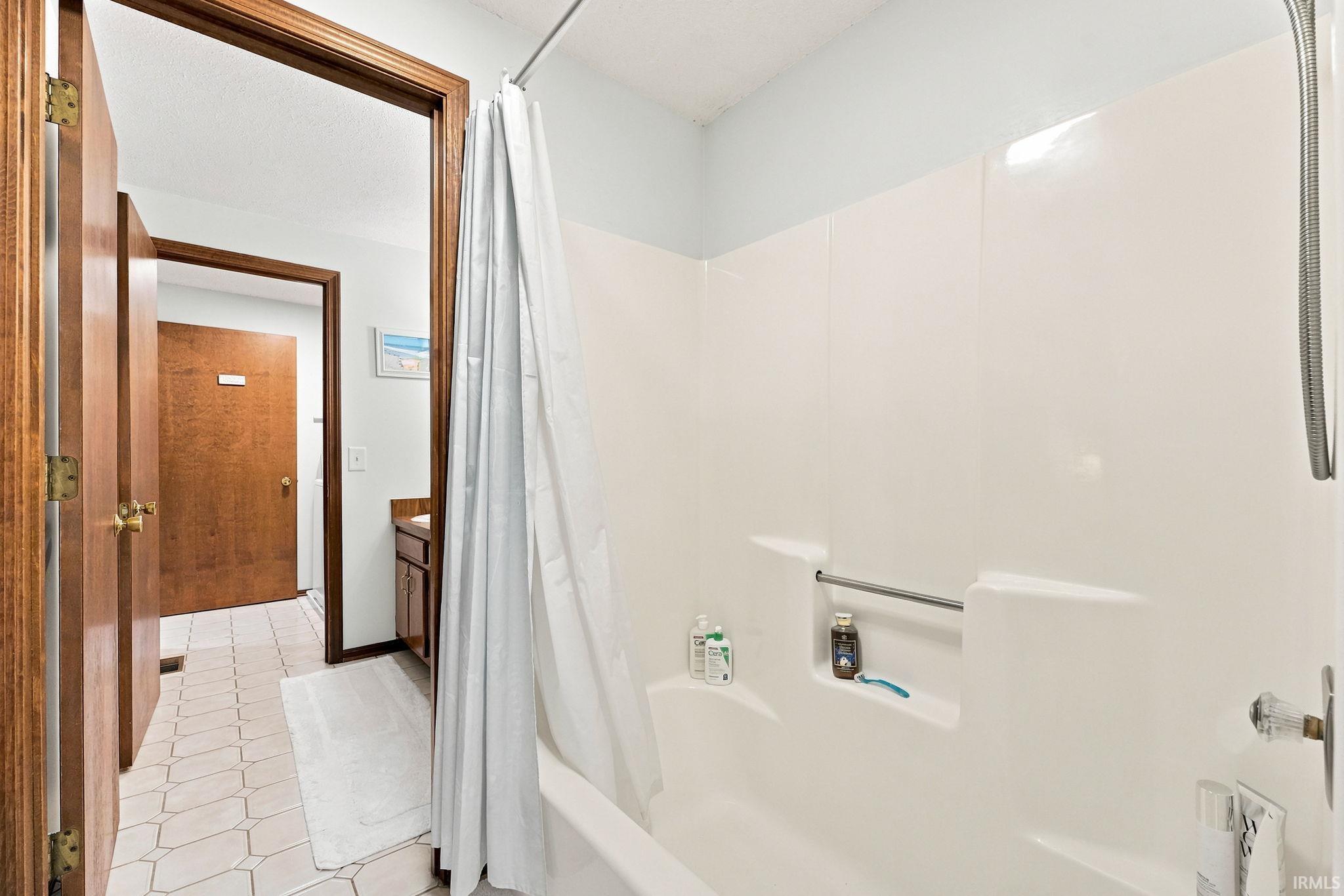 Integrated tub and shower combination with white surround, built-in shelving, and a grab bar
